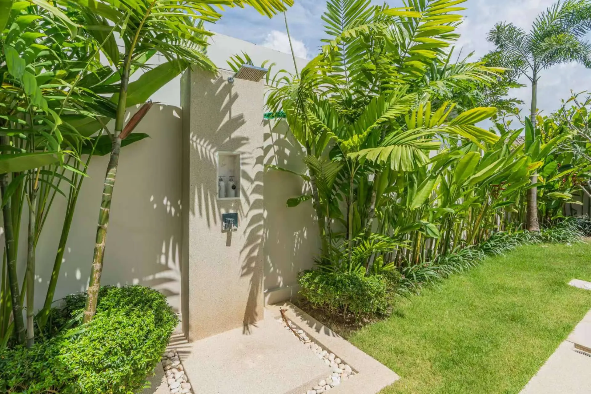 Outdoor shower against a garden wall among palms