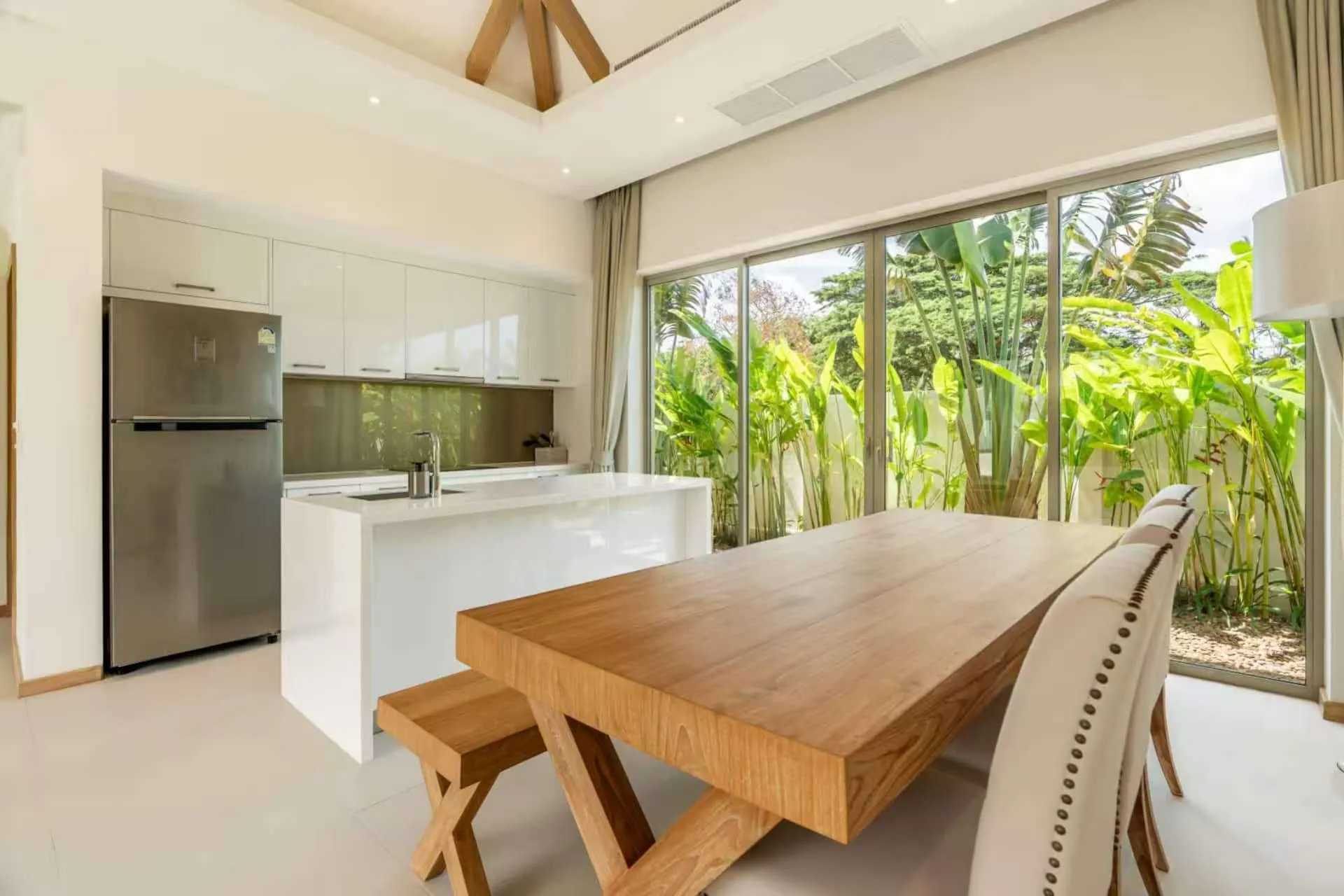 Long wooden dining table beside a white kitchen island, with glass doors to the garden