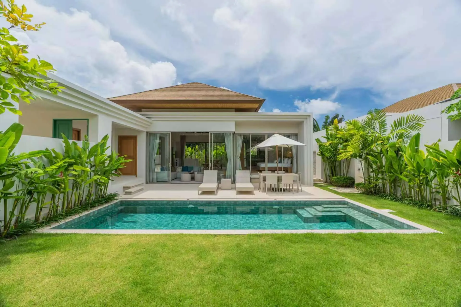 The villa seen across the lawn and pool, with glass doors along the terrace