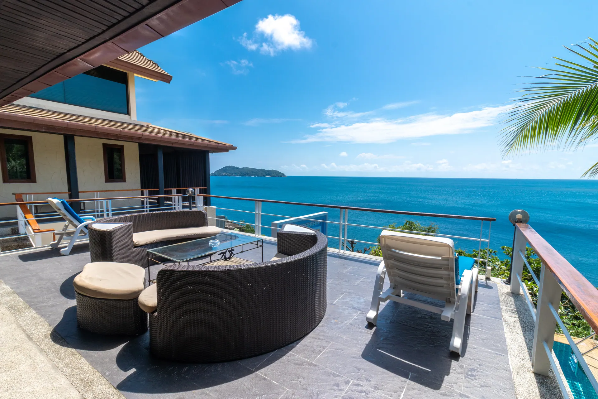 Outdoor lounge on a sea-view terrace with woven sofas and a sun lounger