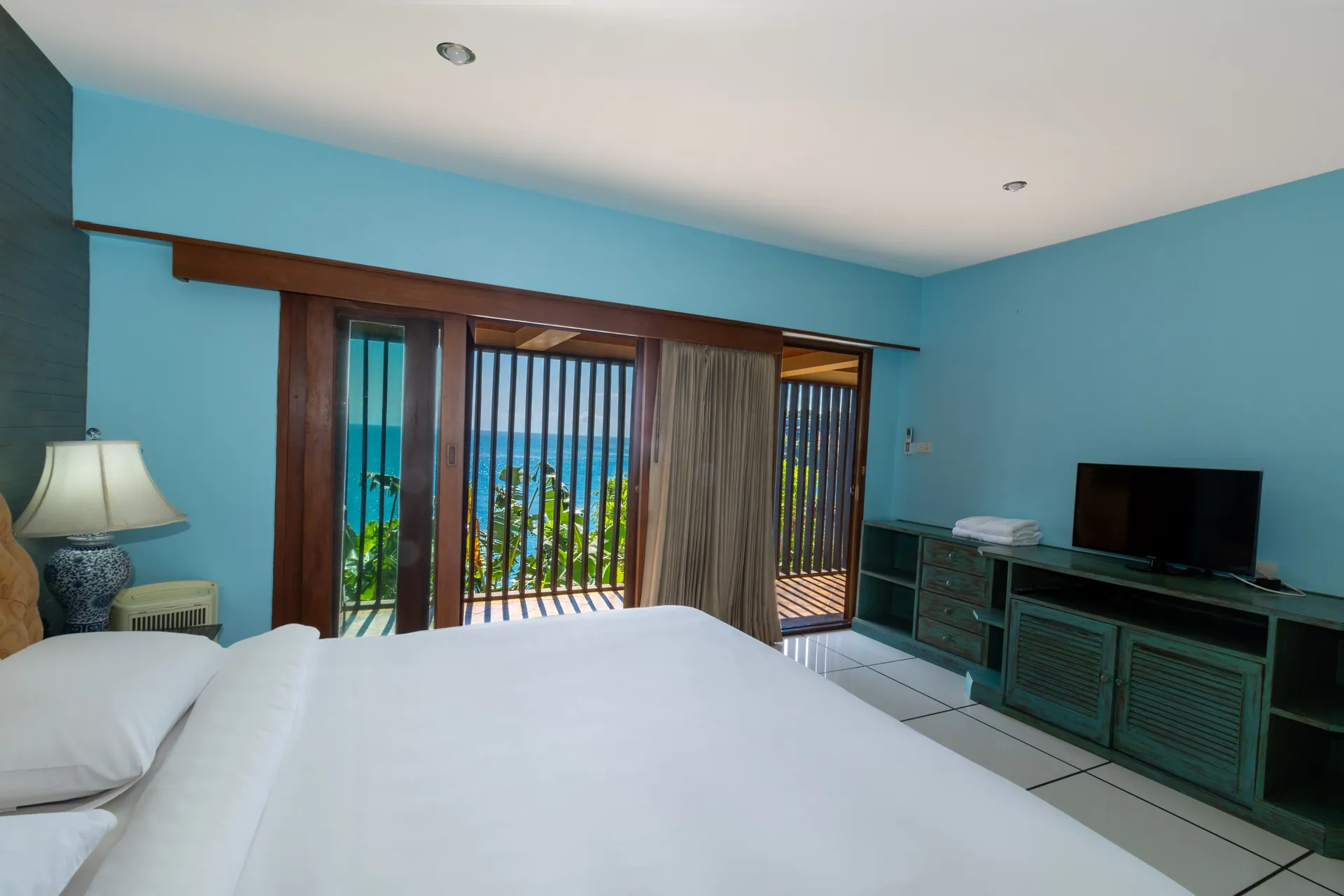 Bedroom with blue walls and a louvred balcony facing the sea