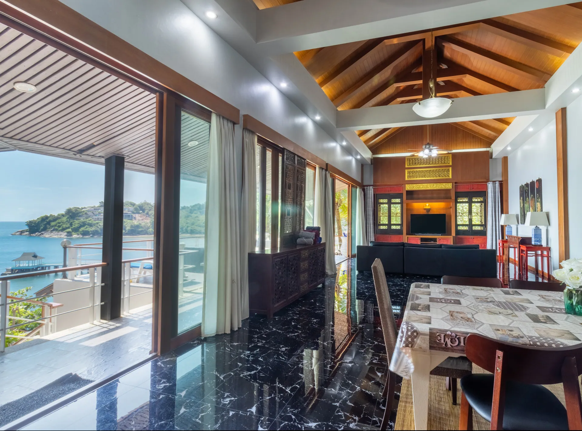 Dining area with a long table beside tall windows facing the sea