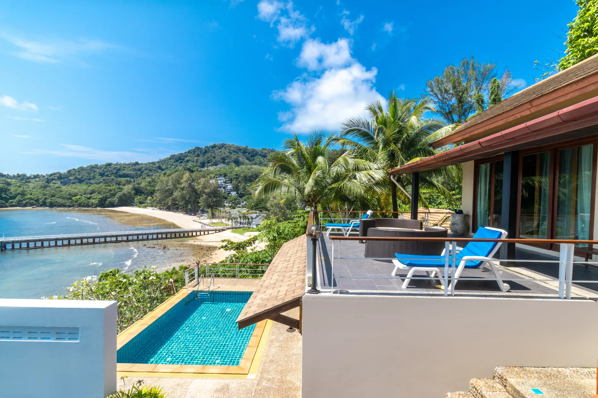Upper sun deck with loungers above the pool, overlooking the bay, a long pier and the beach