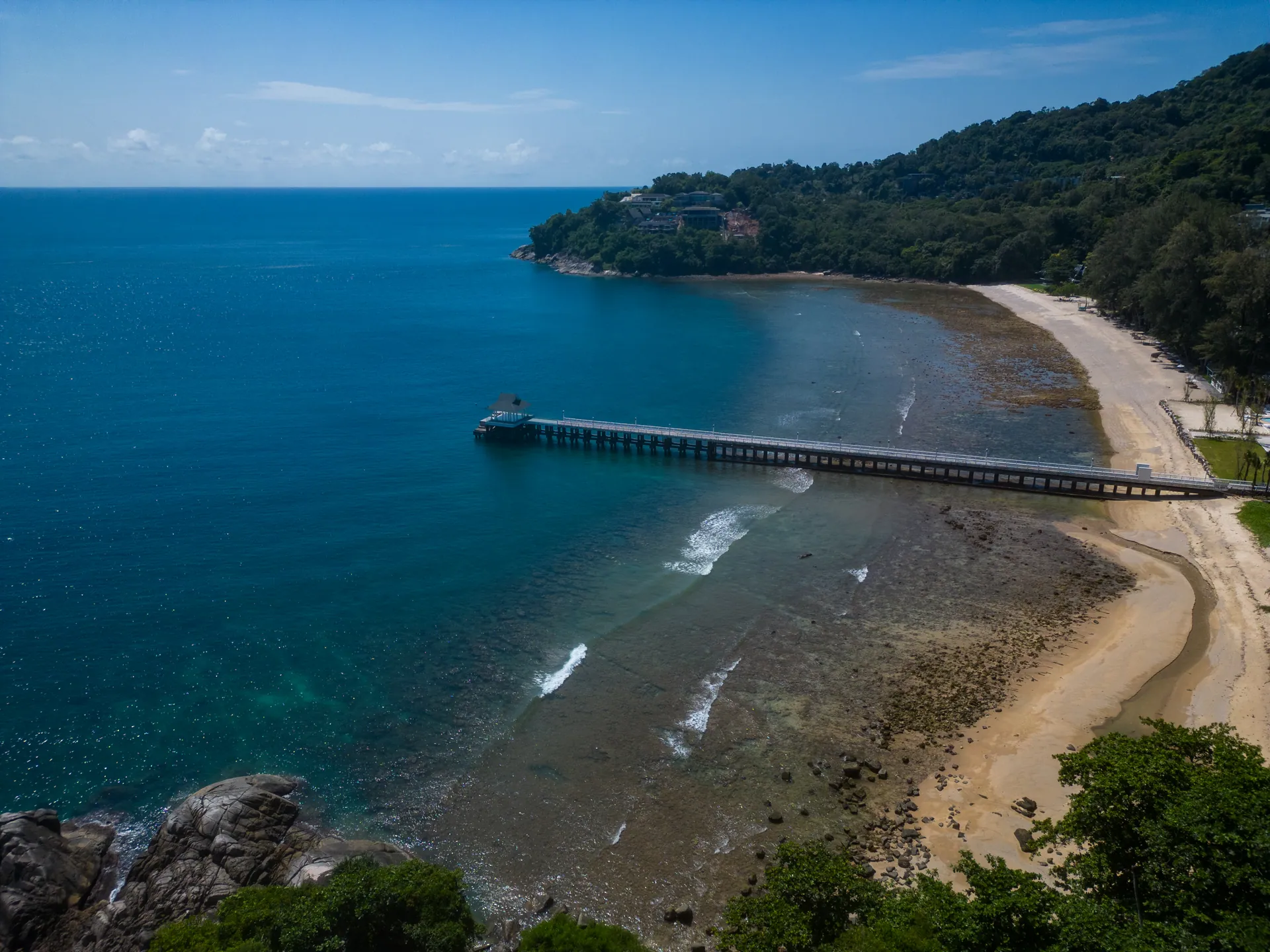 Aerial view of the nearby bay, with a long pier and a curving sandy beach