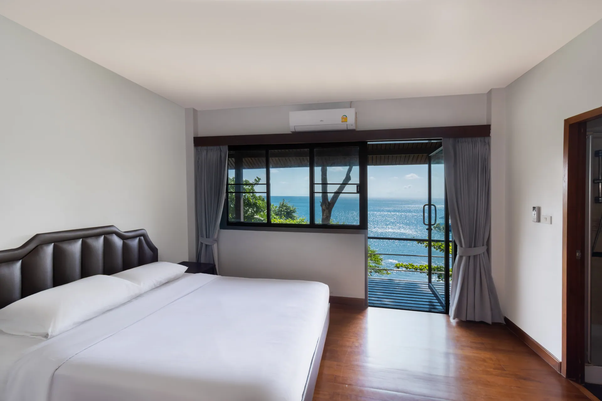 Bedroom with a large bed, wooden floor and a balcony door facing the sea