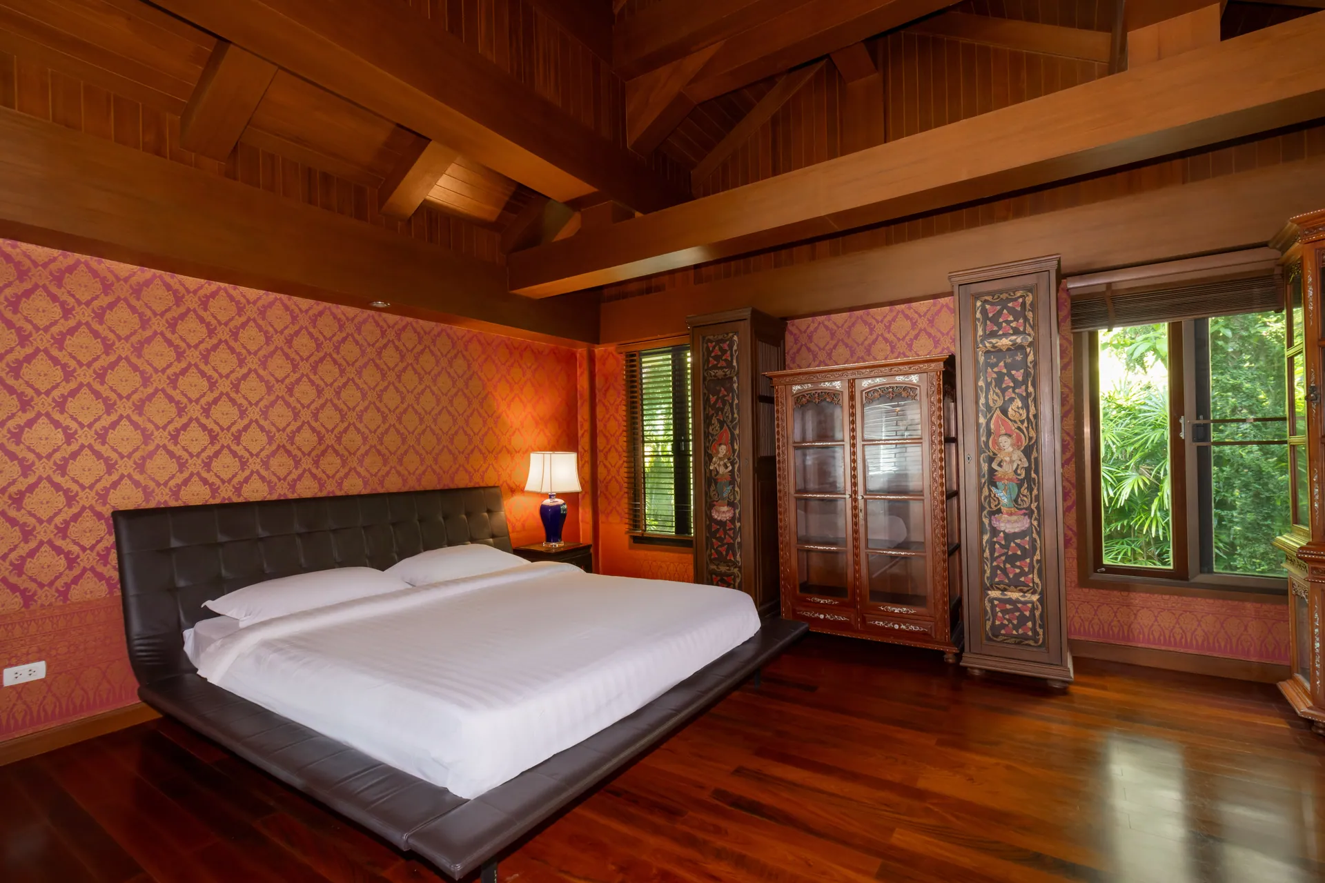 Thai-style bedroom with a timber ceiling, patterned walls and carved wooden cabinets