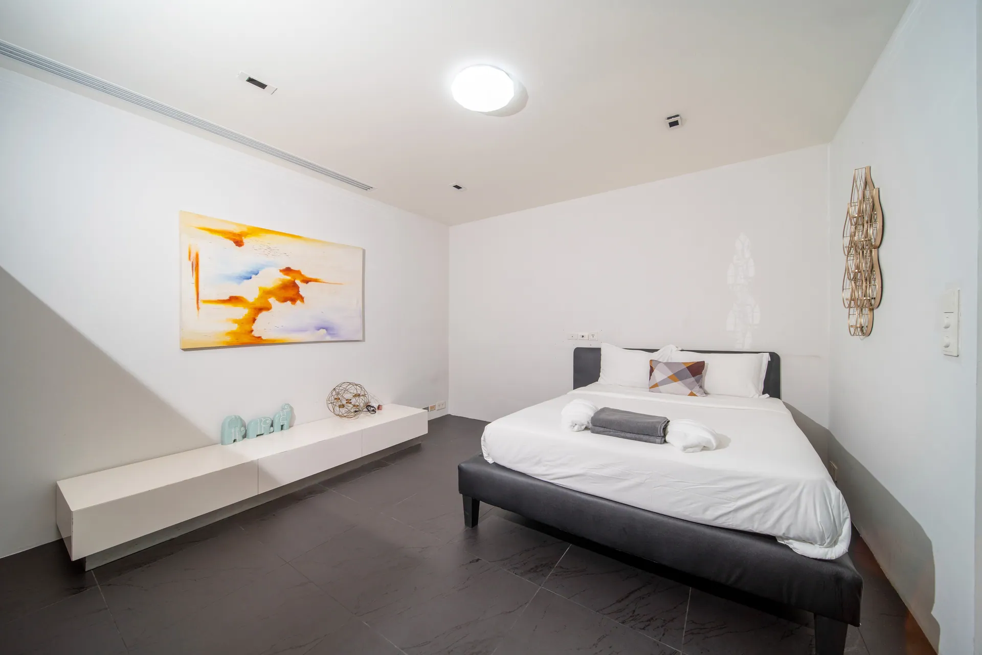 Bedroom with a dark bed frame, a low white console and a painting in warm tones