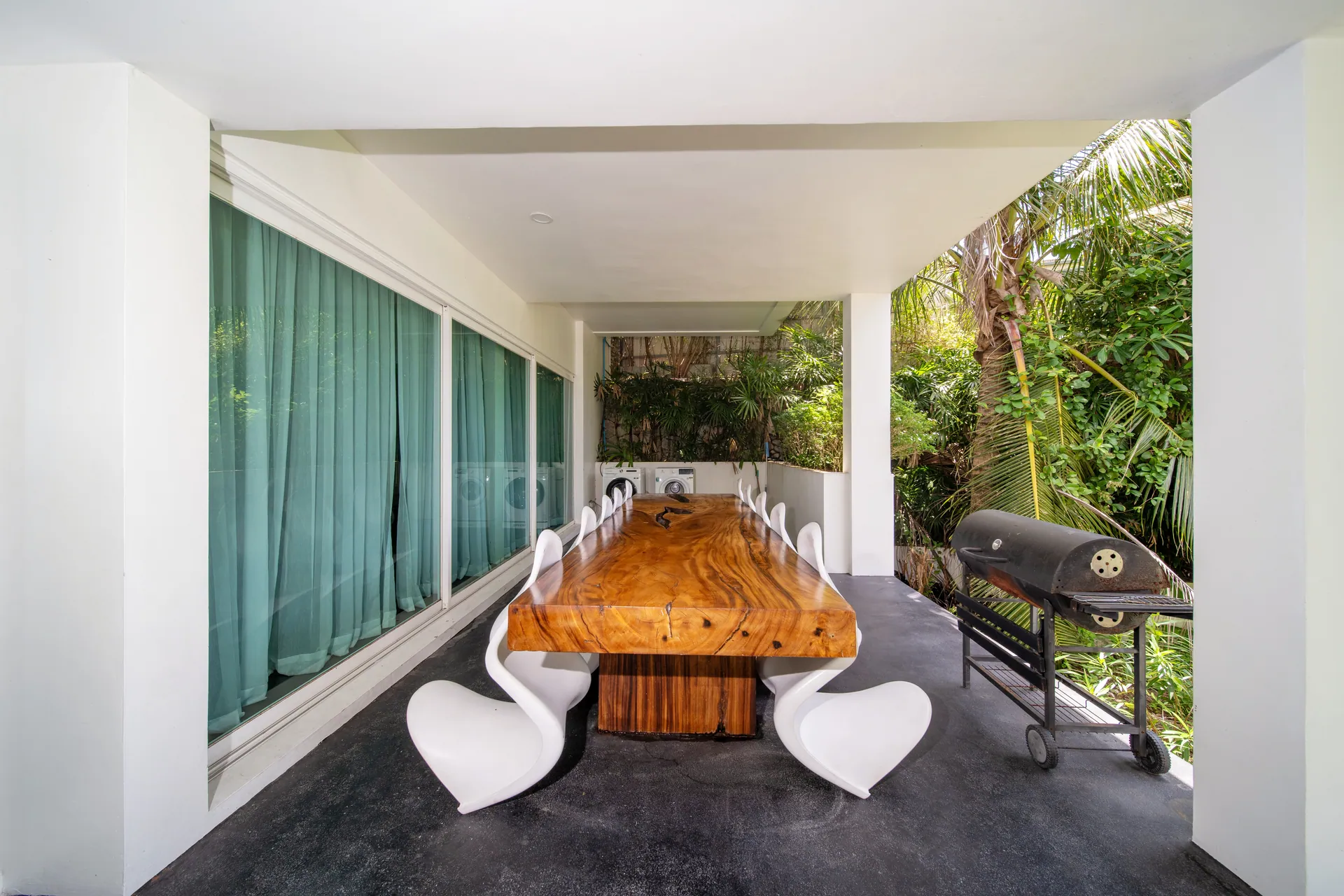 Covered terrace with a long timber dining table, white chairs and a barbecue grill