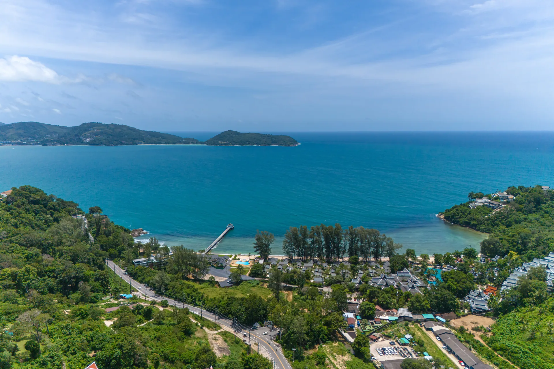Aerial view over the green hills to a bay with a pier, a sandy beach and the open sea