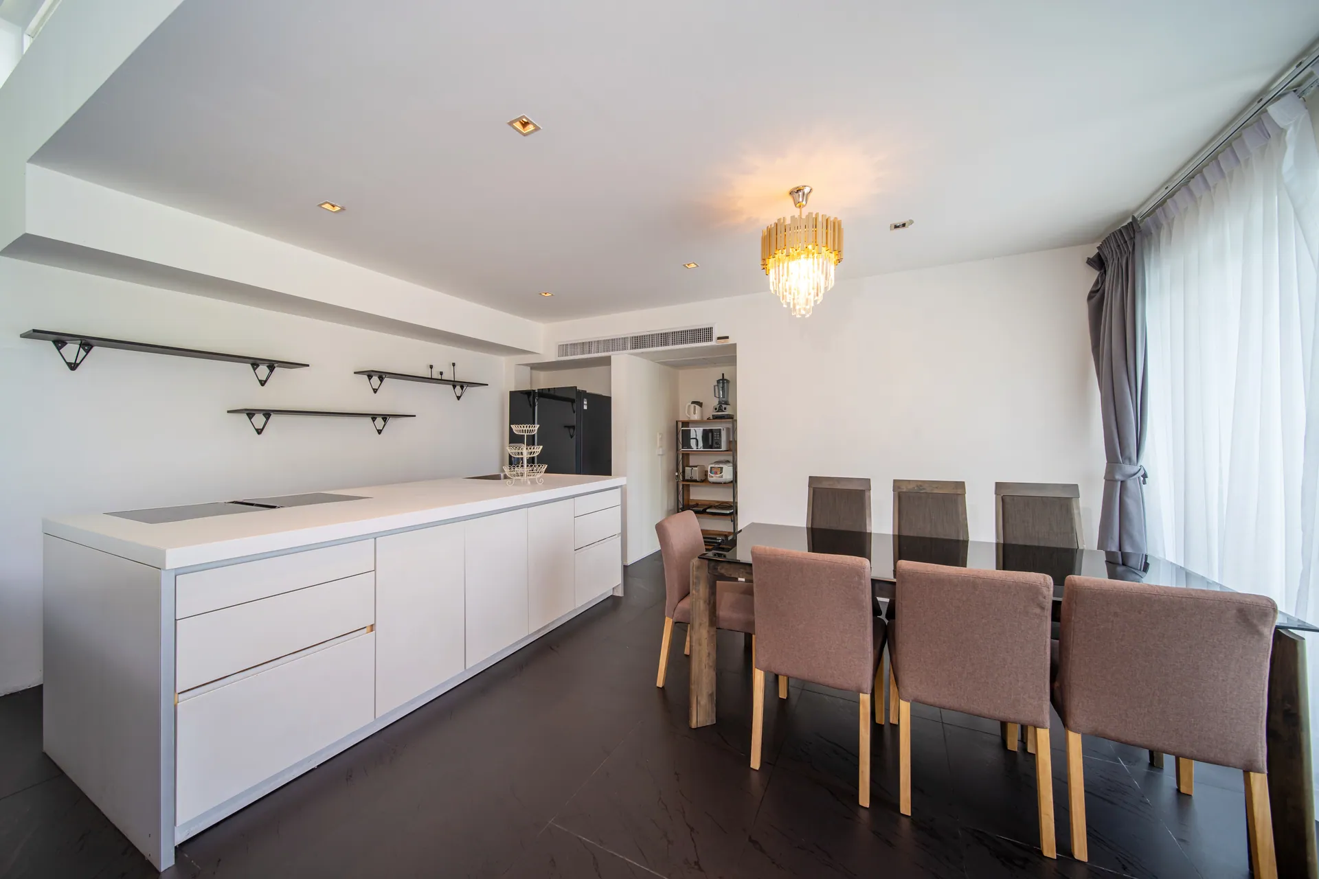 Fitted kitchen with a long white counter beside the dining table and a crystal pendant light