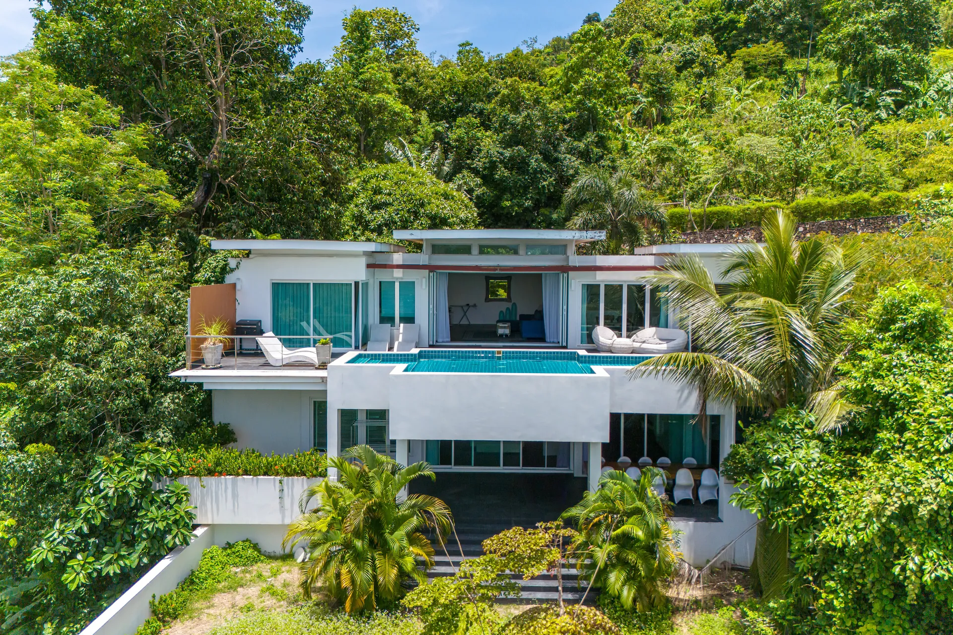 Aerial view of the white, multi-level villa set into the forested hillside