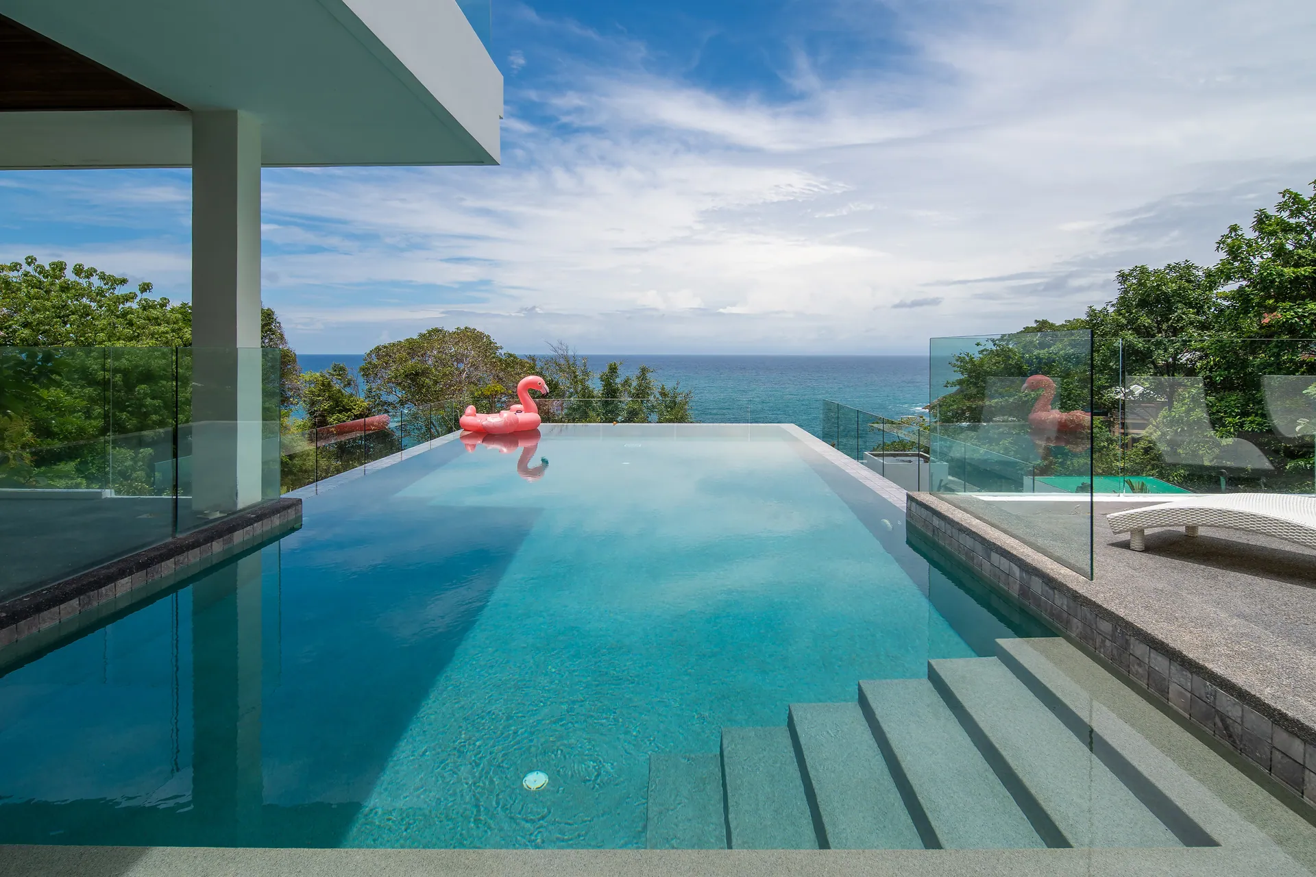 Infinity-edge pool with entry steps, looking out over the treetops to the sea