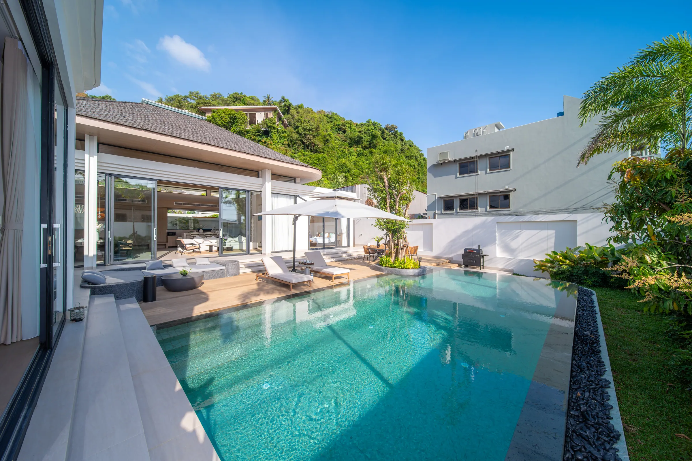 Private pool beside the timber deck, with the glass-fronted living pavilion open behind it and a wooded hill beyond