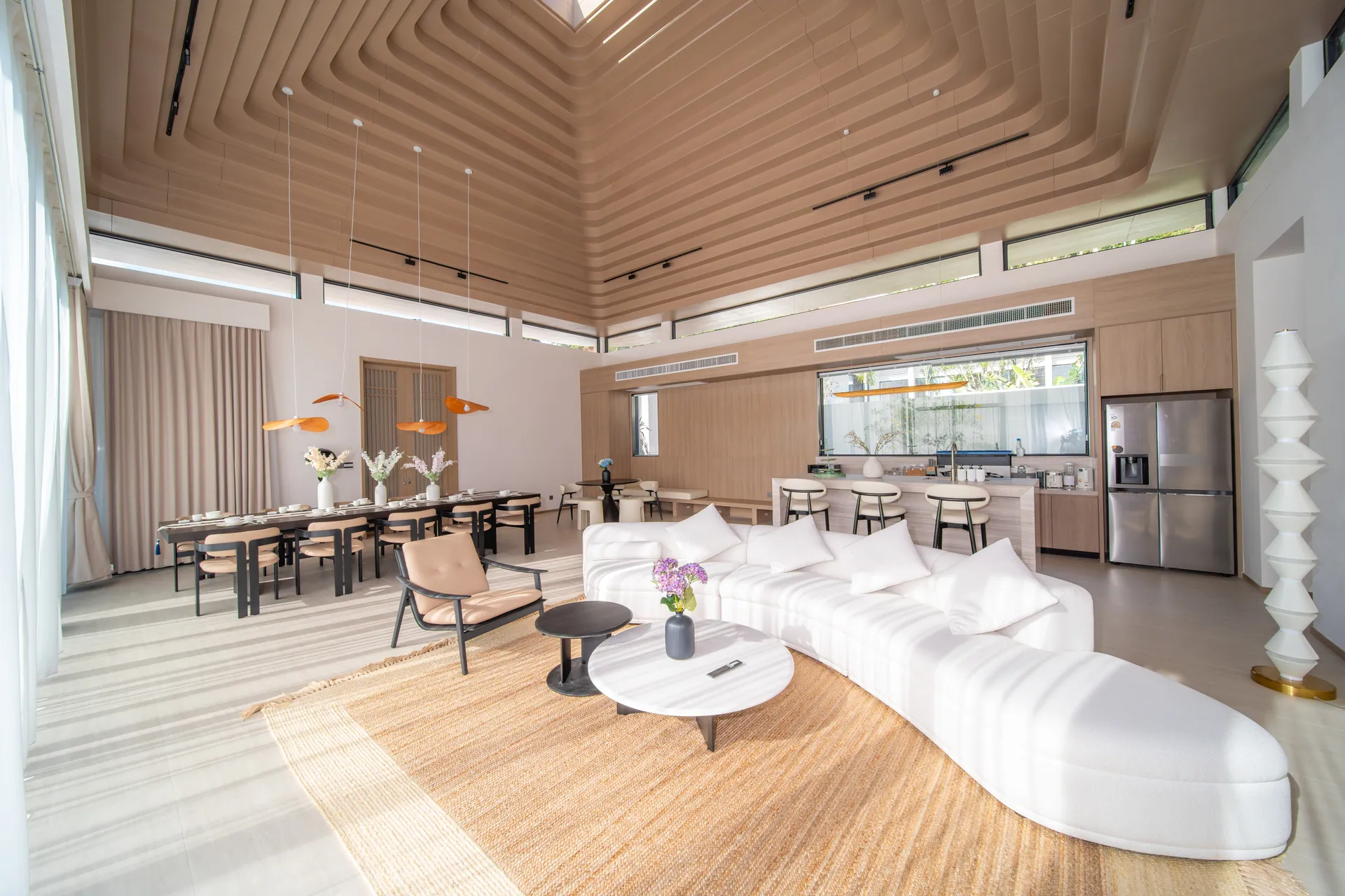 Open-plan living room with a curved white sofa, the dining table and the kitchen beyond