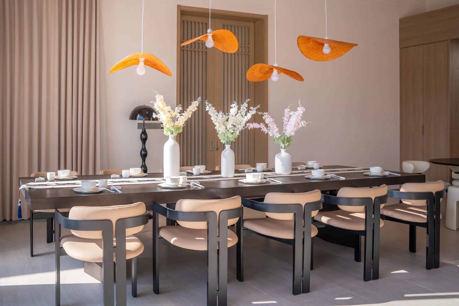 Long dining table set beneath woven orange pendant lights
