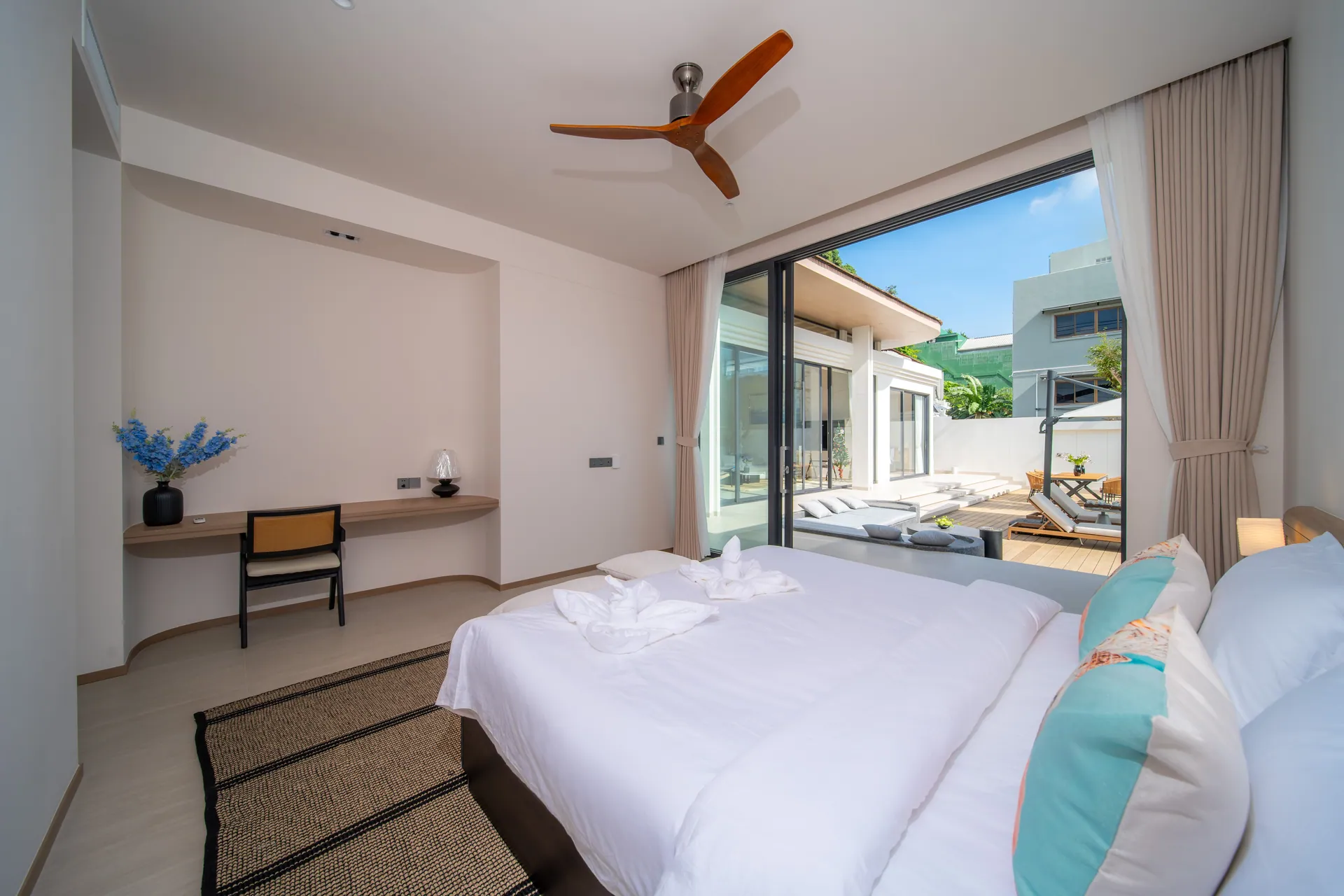 Bedroom with a king bed and a built-in writing desk, its glass wall open to the pool deck
