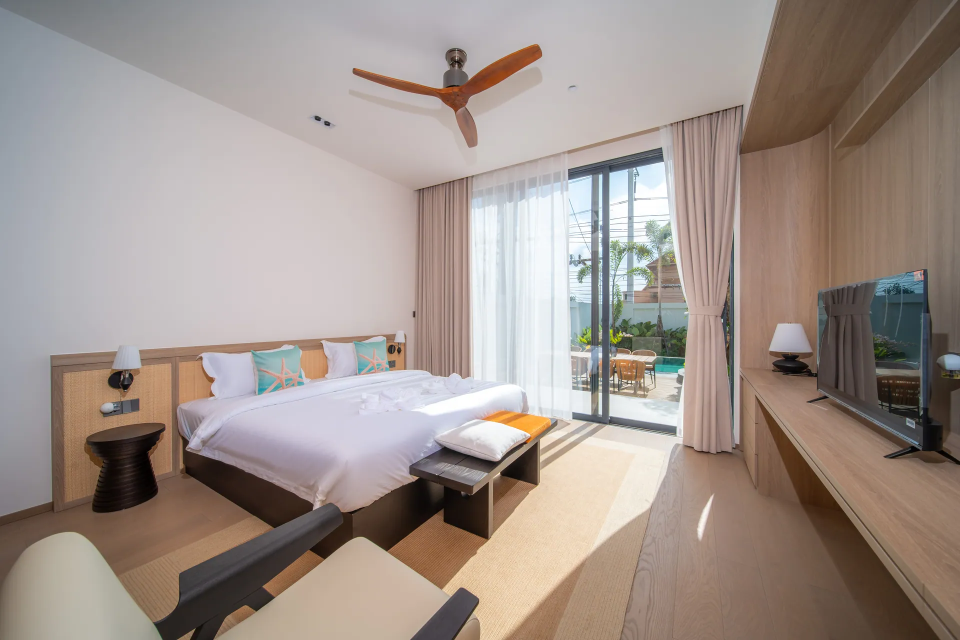 Bedroom with a king bed, an armchair and a television, with the pool deck outside