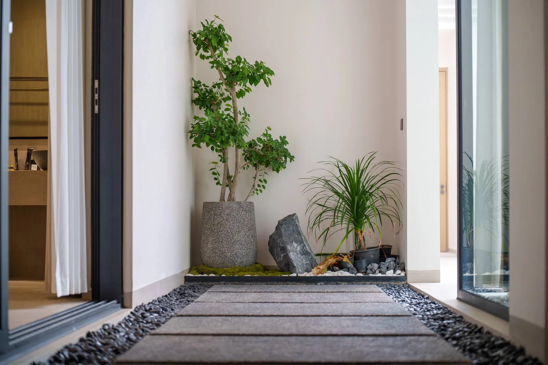 Small planted courtyard with stepping stones and pebbles between glass doors