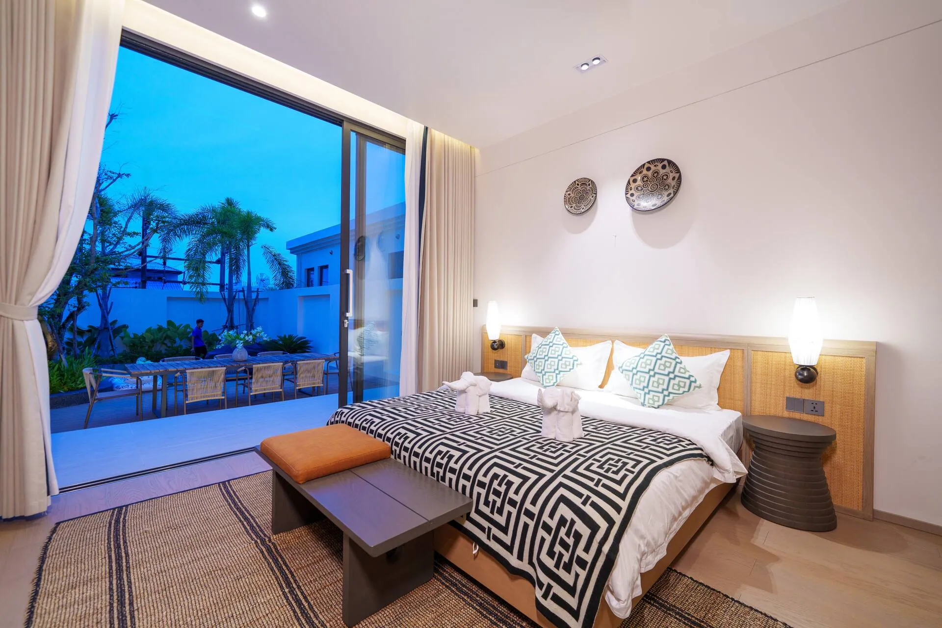 King bed below woven wall plates, with glass doors to the pool deck at dusk