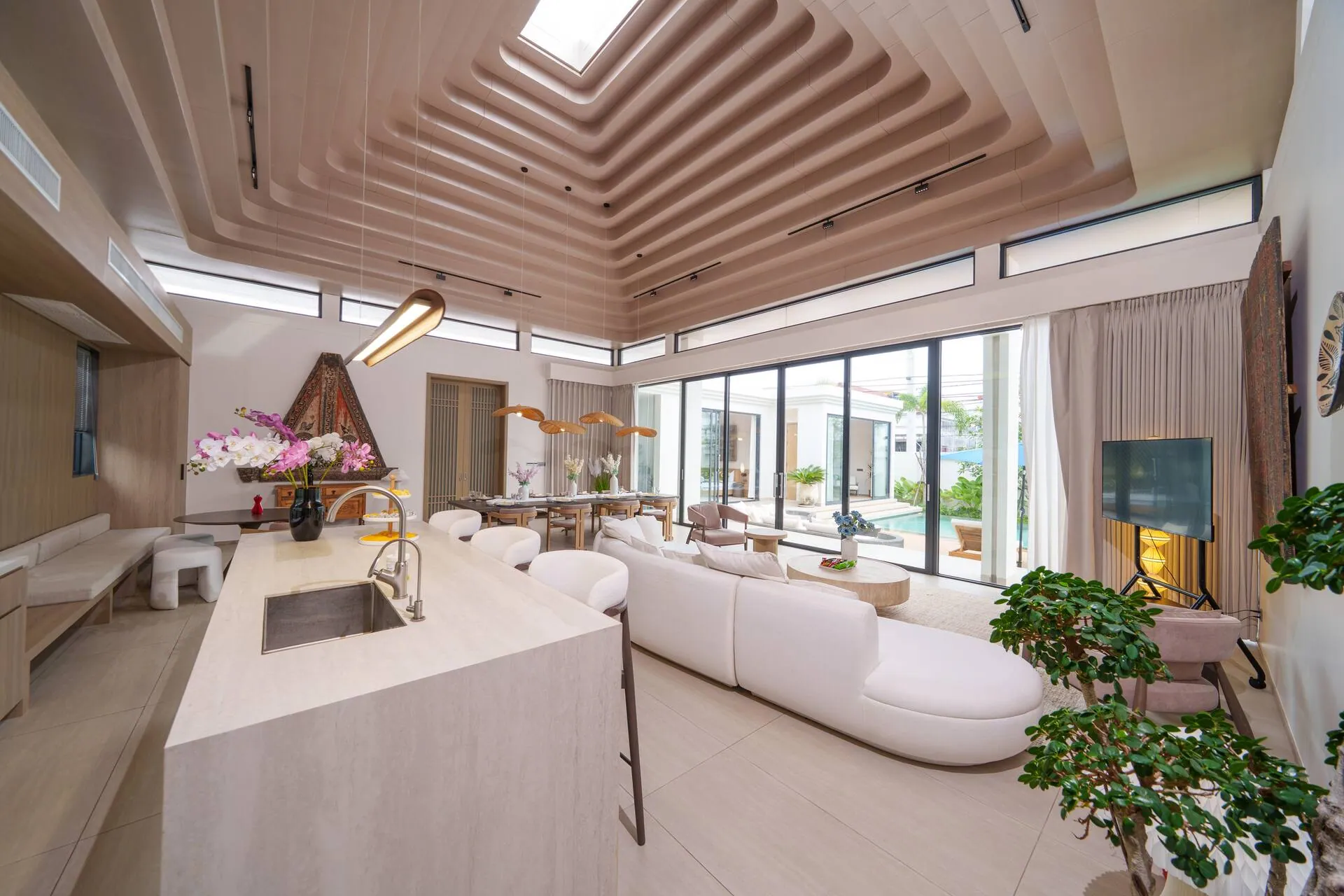 Open-plan living room beneath a stepped timber ceiling and skylight, with the kitchen island in front