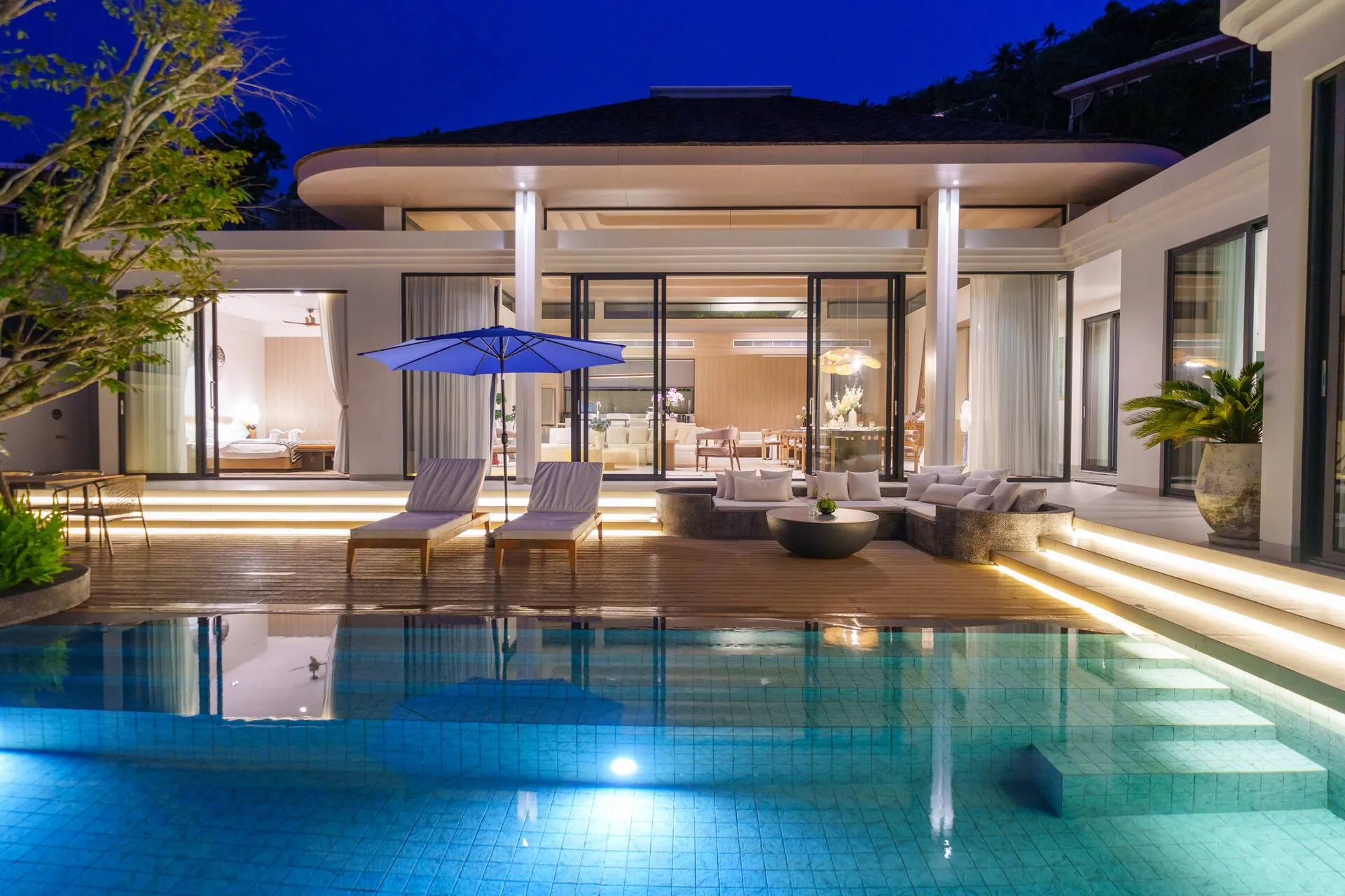 Private pool at dusk, lit from below, in front of the glass-walled living pavilion