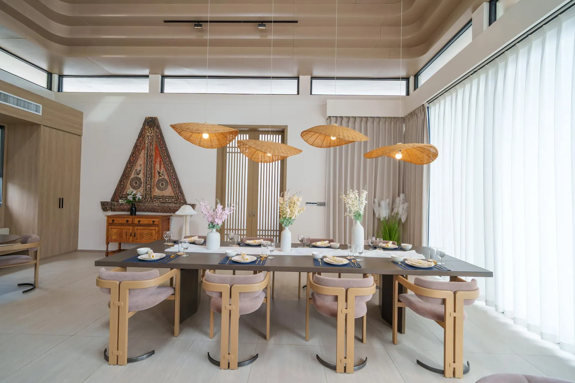 Dining table beneath woven pendant lights, in front of a carved triangular timber panel