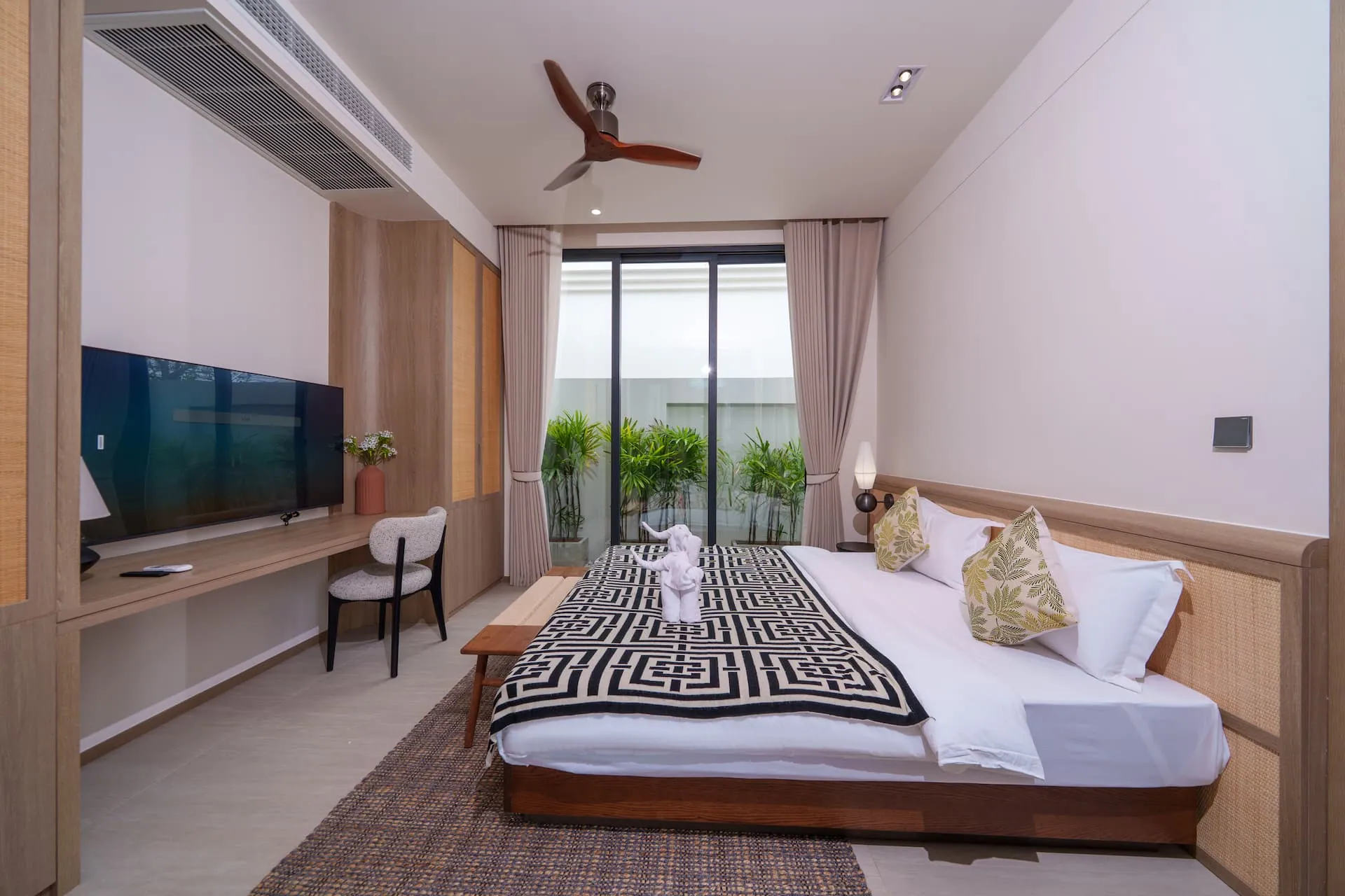 Bedroom with a king bed, a desk and a wall-mounted television, and glass doors opening onto a planted border