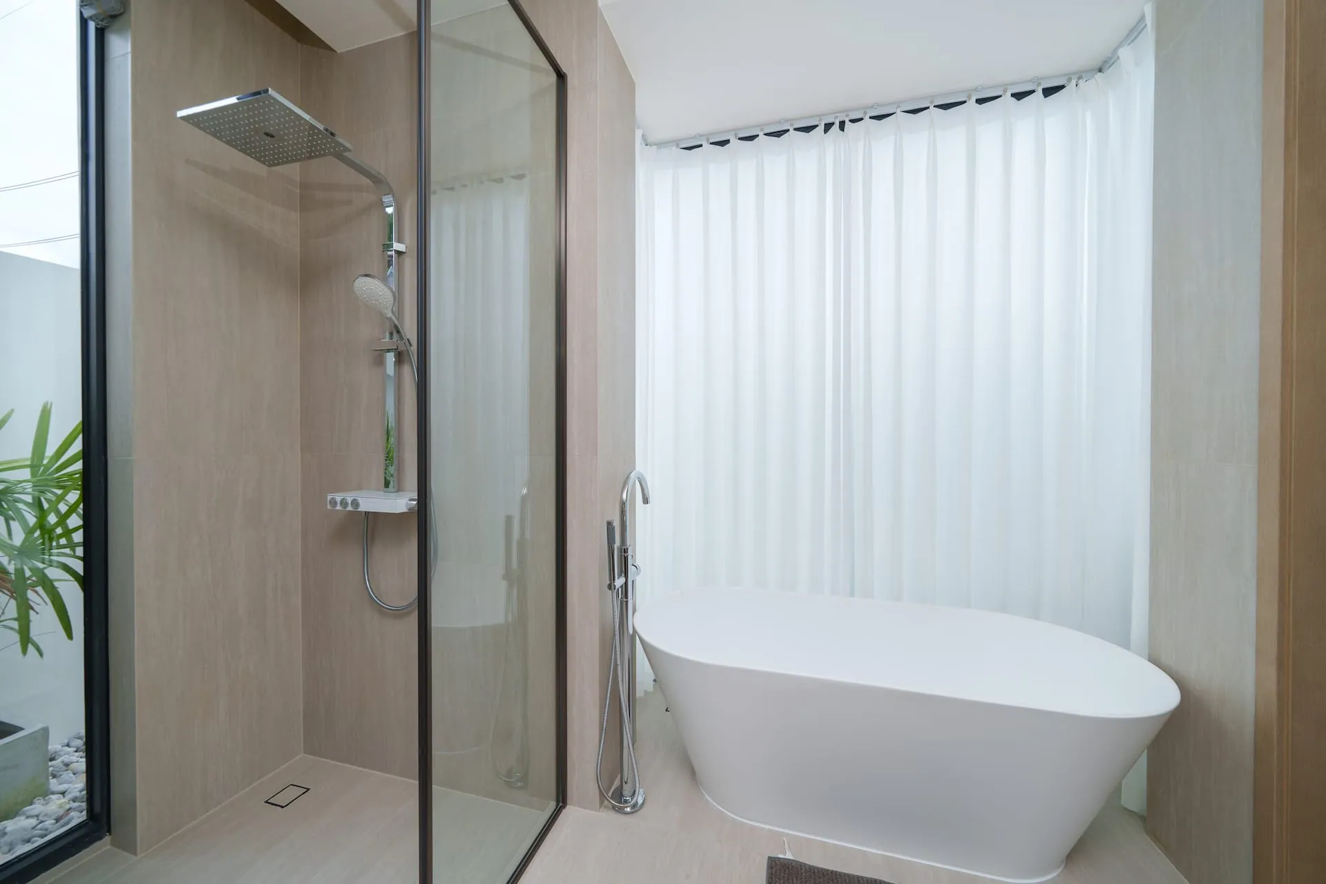 Freestanding bath beside a glass-walled rain shower, screened by sheer curtains