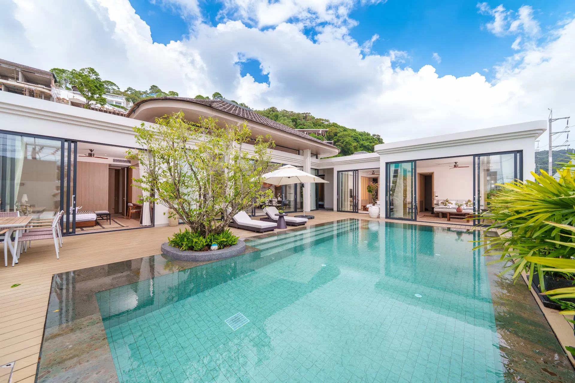 Wide view across the pool to the bedroom wings, with a tree planted at the pool's edge