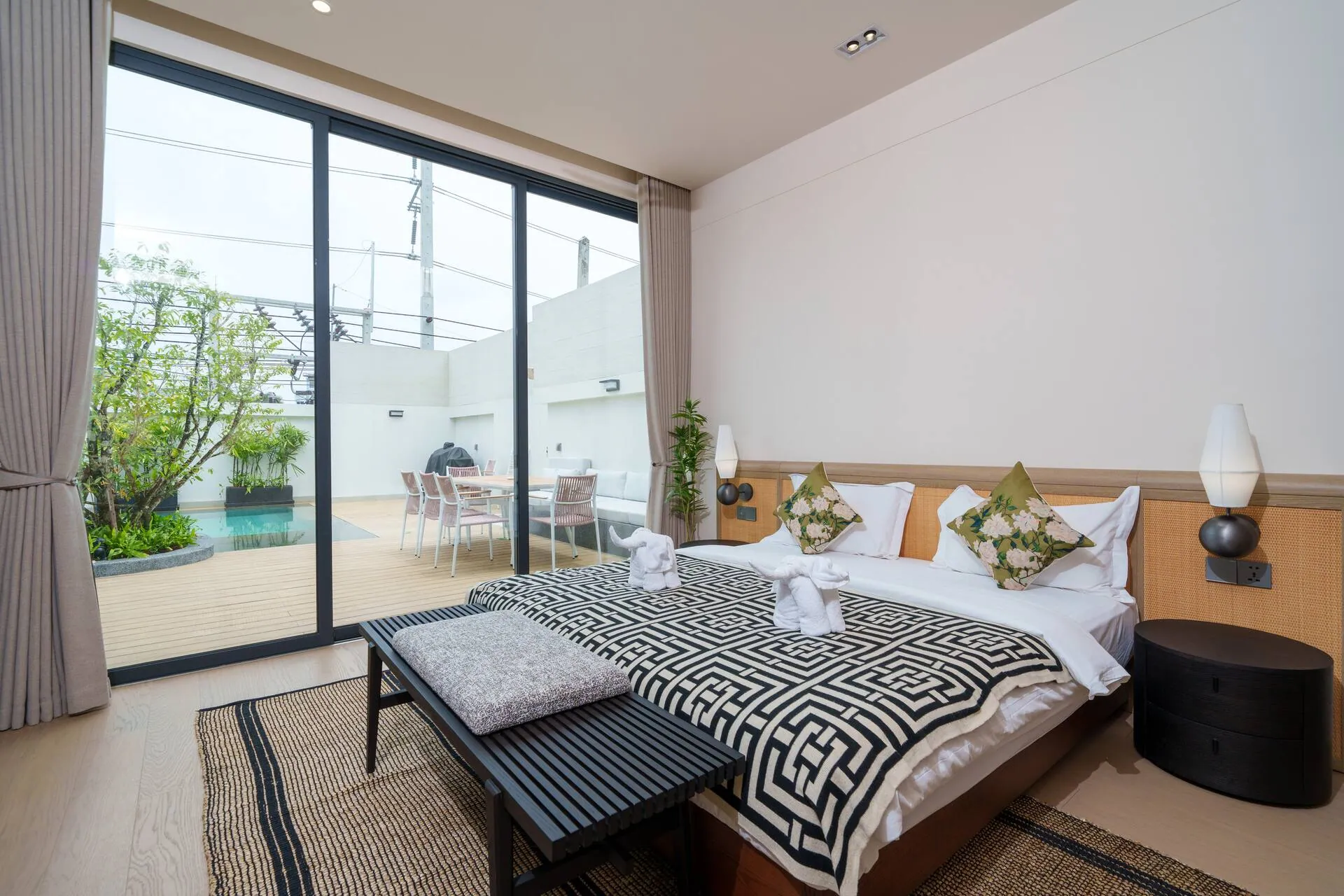 Bedroom with a king bed and a glass wall onto the pool garden and outdoor dining terrace