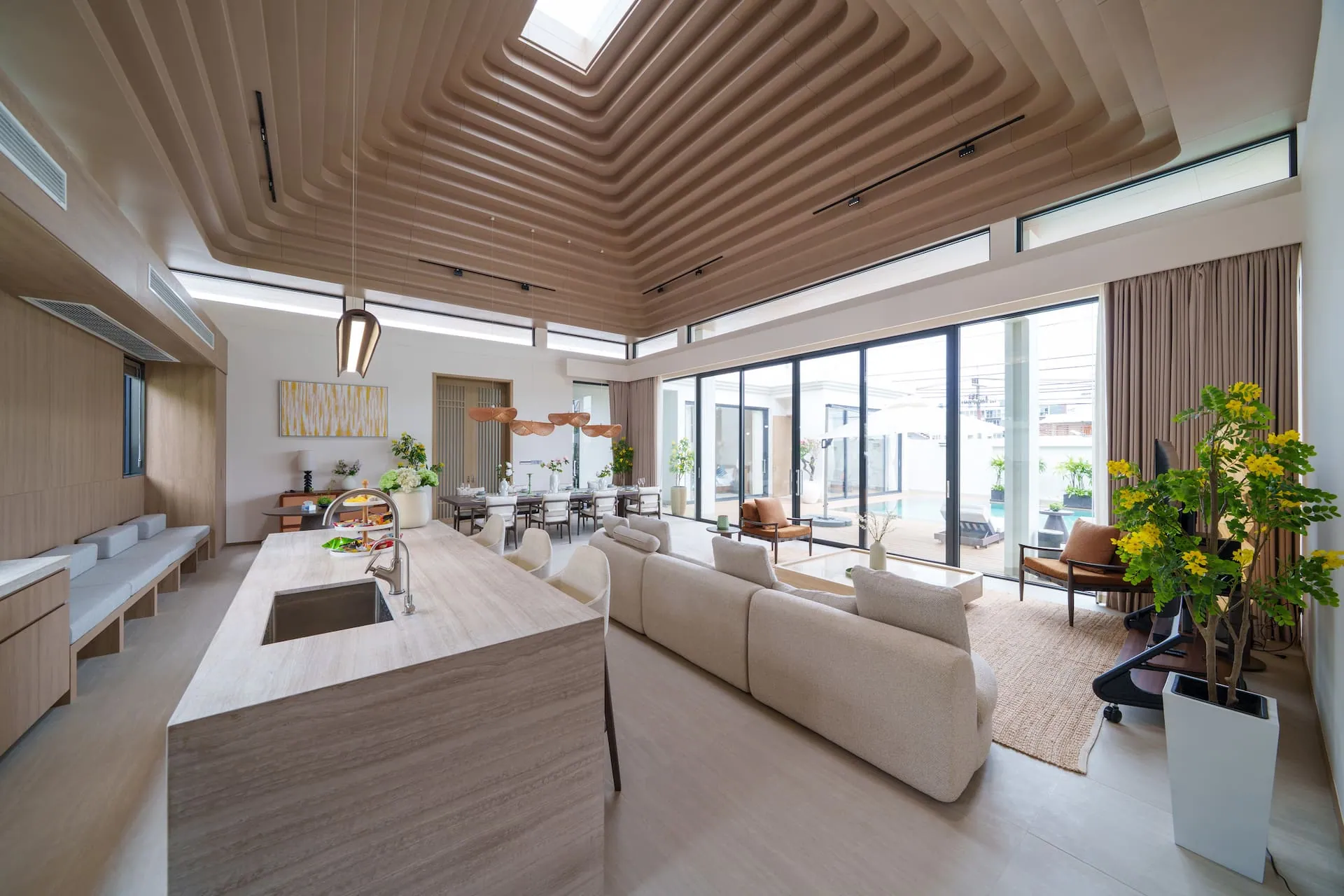 Open-plan pavilion with the kitchen island in the foreground and a stepped timber ceiling rising to a skylight