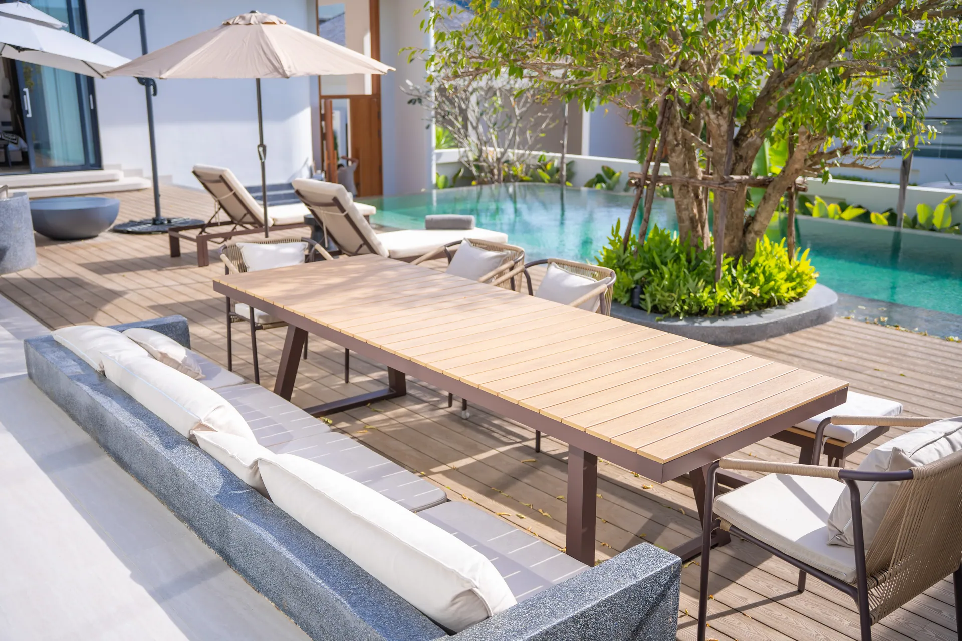 Outdoor dining table and built-in sofa on the deck, beside the pool and the courtyard tree