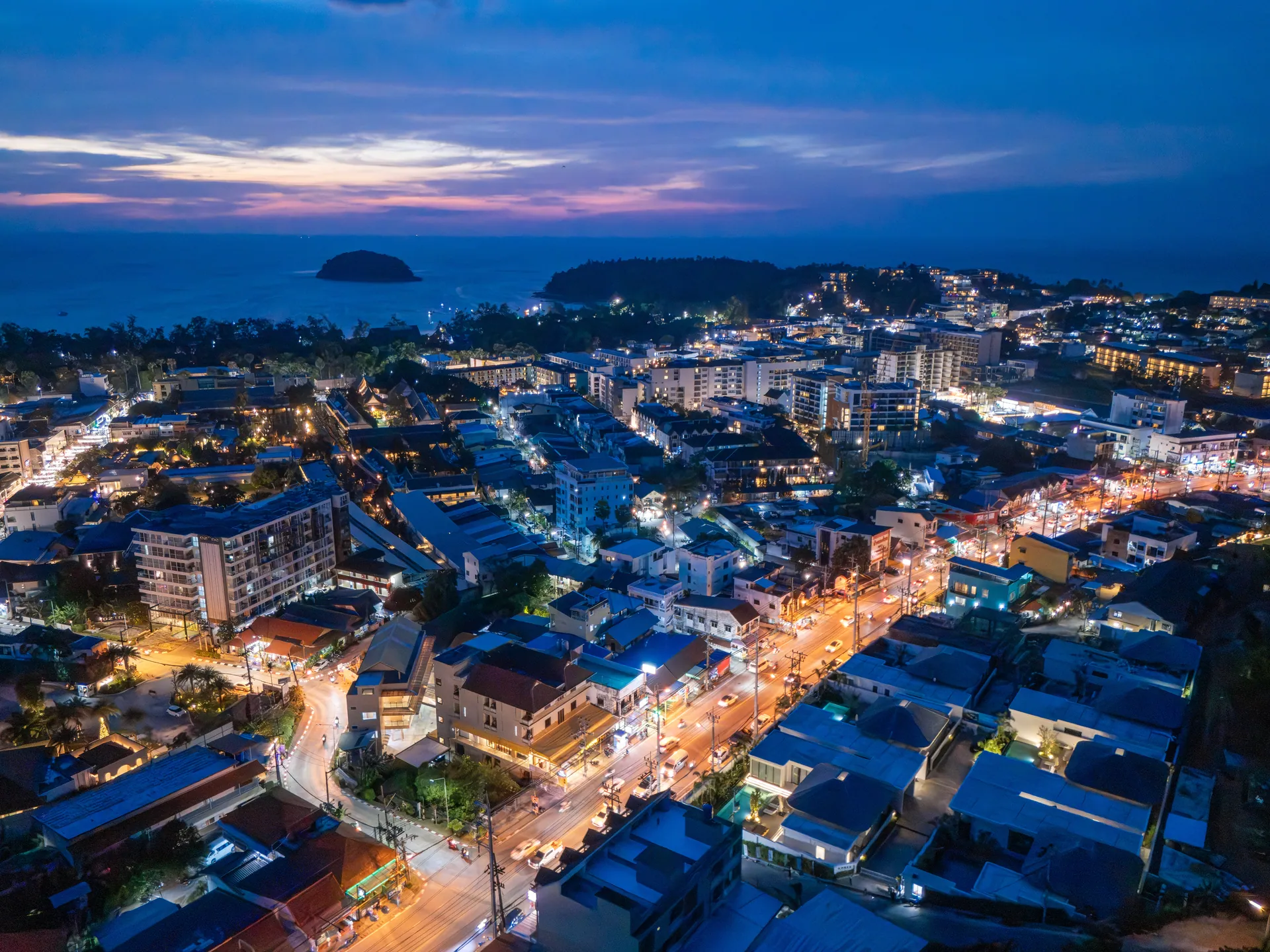 Kata from the air at dusk, with the lights of the town, the bay and a small island offshore