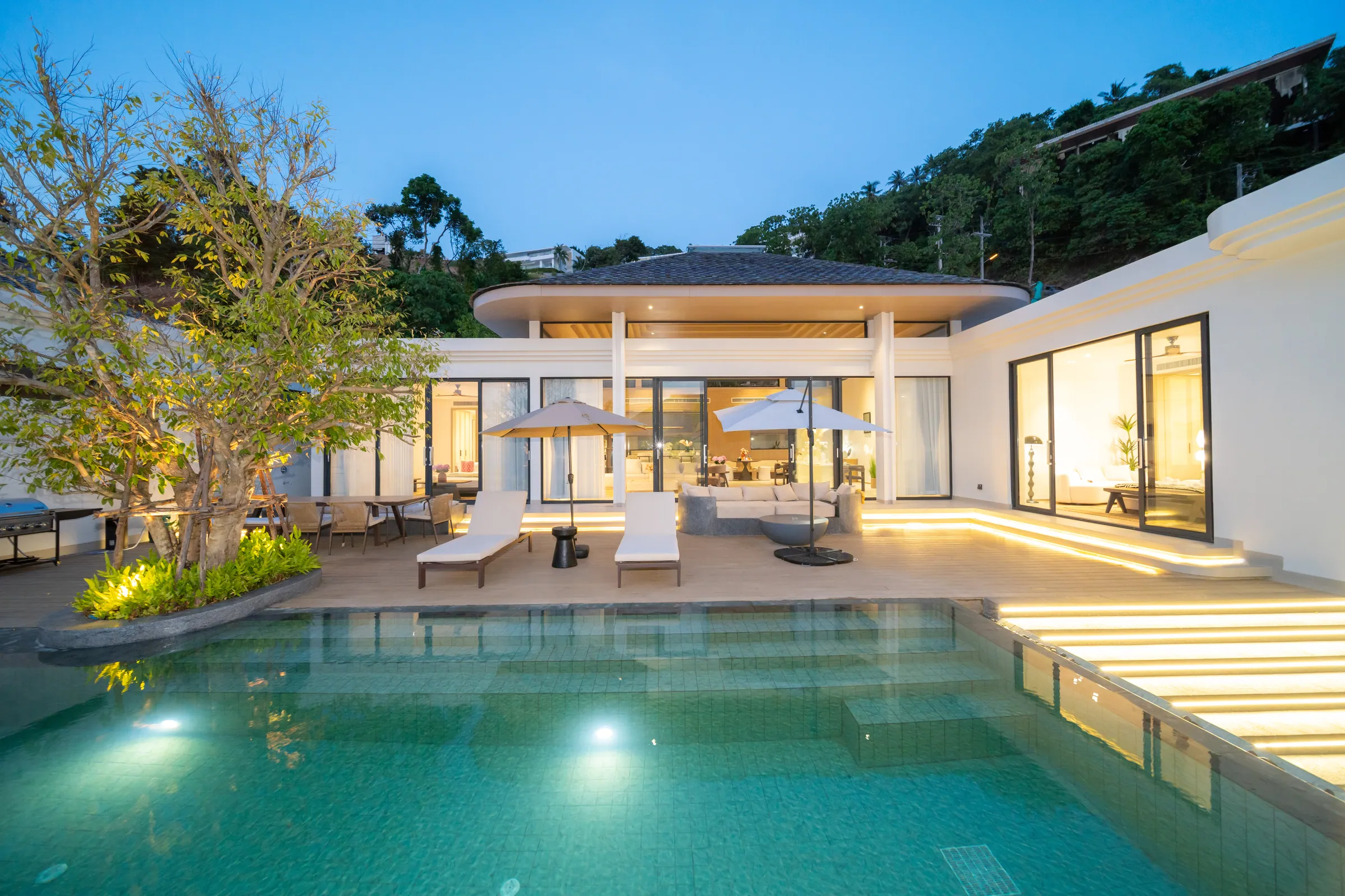 Courtyard pool at dusk, lit from below, with sun loungers on the terrace and the living pavilion behind