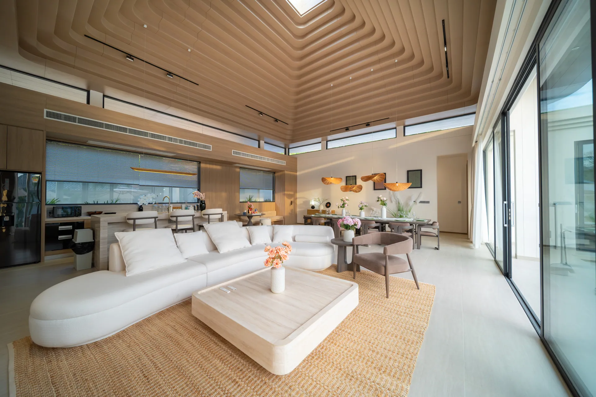 Open-plan living room with a curved white sofa beneath a stepped timber ceiling, with glass doors to the terrace