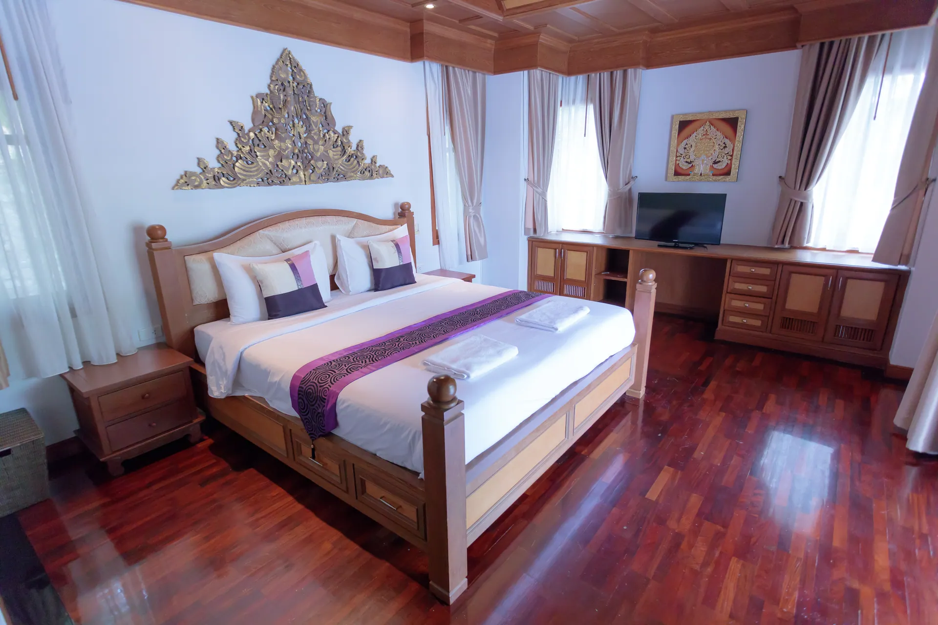 Bedroom 2 with a king bed beneath a gilded Thai carving, desk and TV