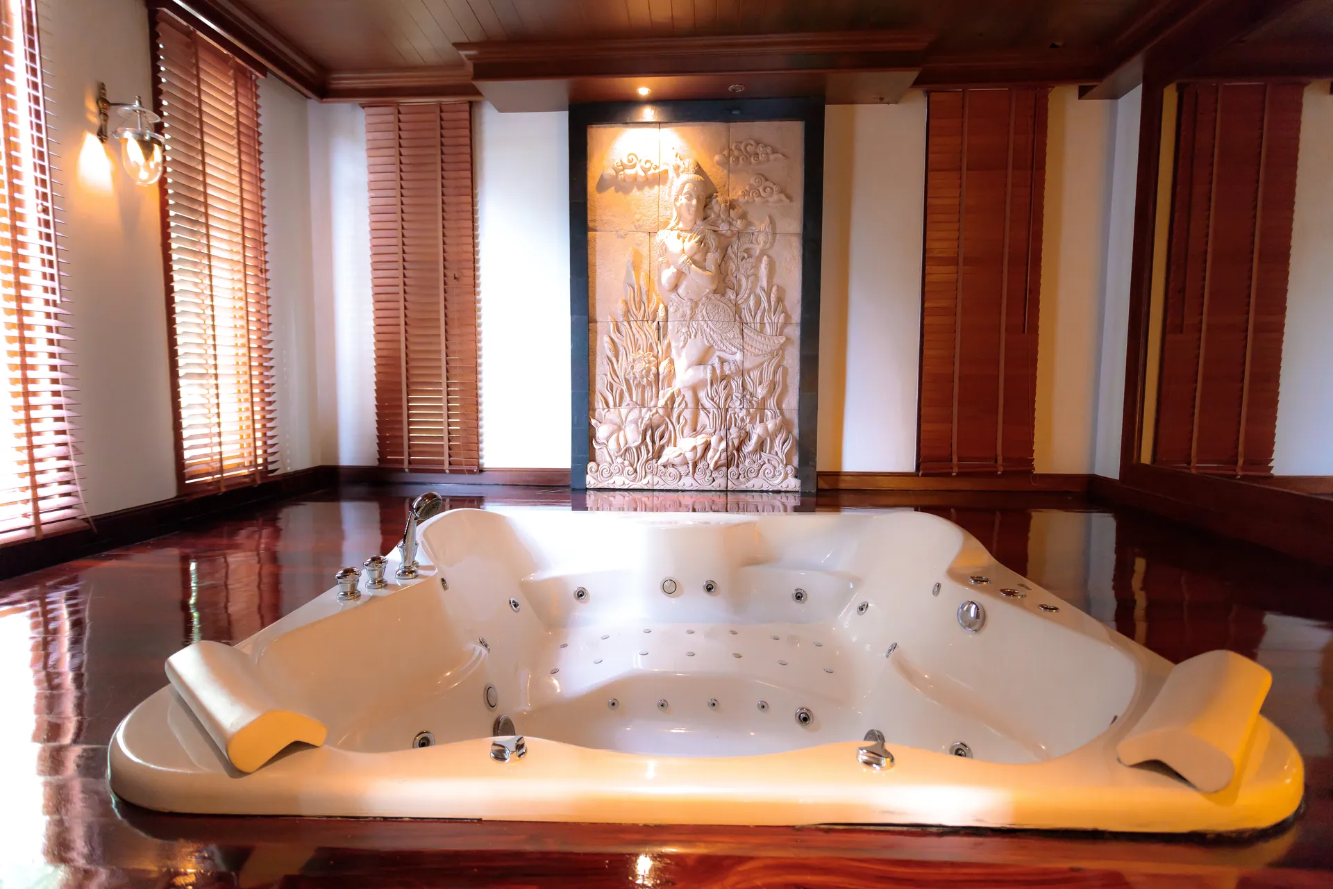 Large jetted tub on a hardwood floor beneath a carved stone relief
