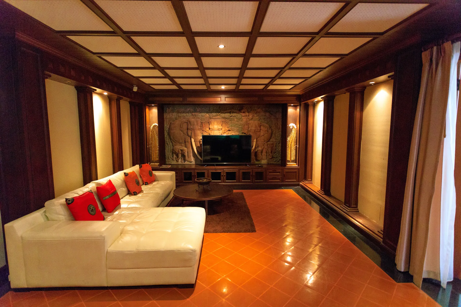 Living room with a white sectional sofa, coffered timber ceiling and carved relief behind the TV