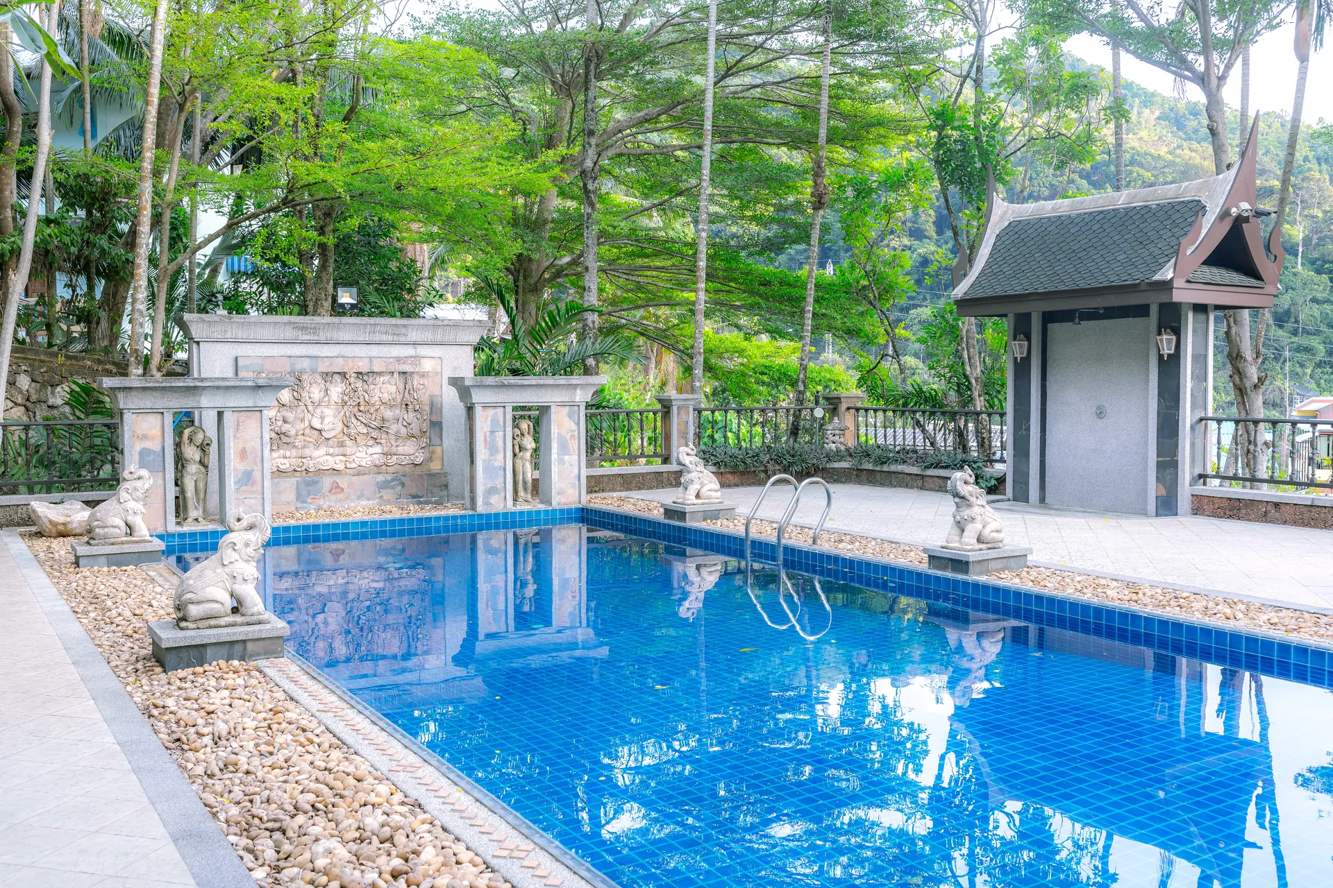 Private pool with a carved stone water wall and a small Thai pavilion among tall trees