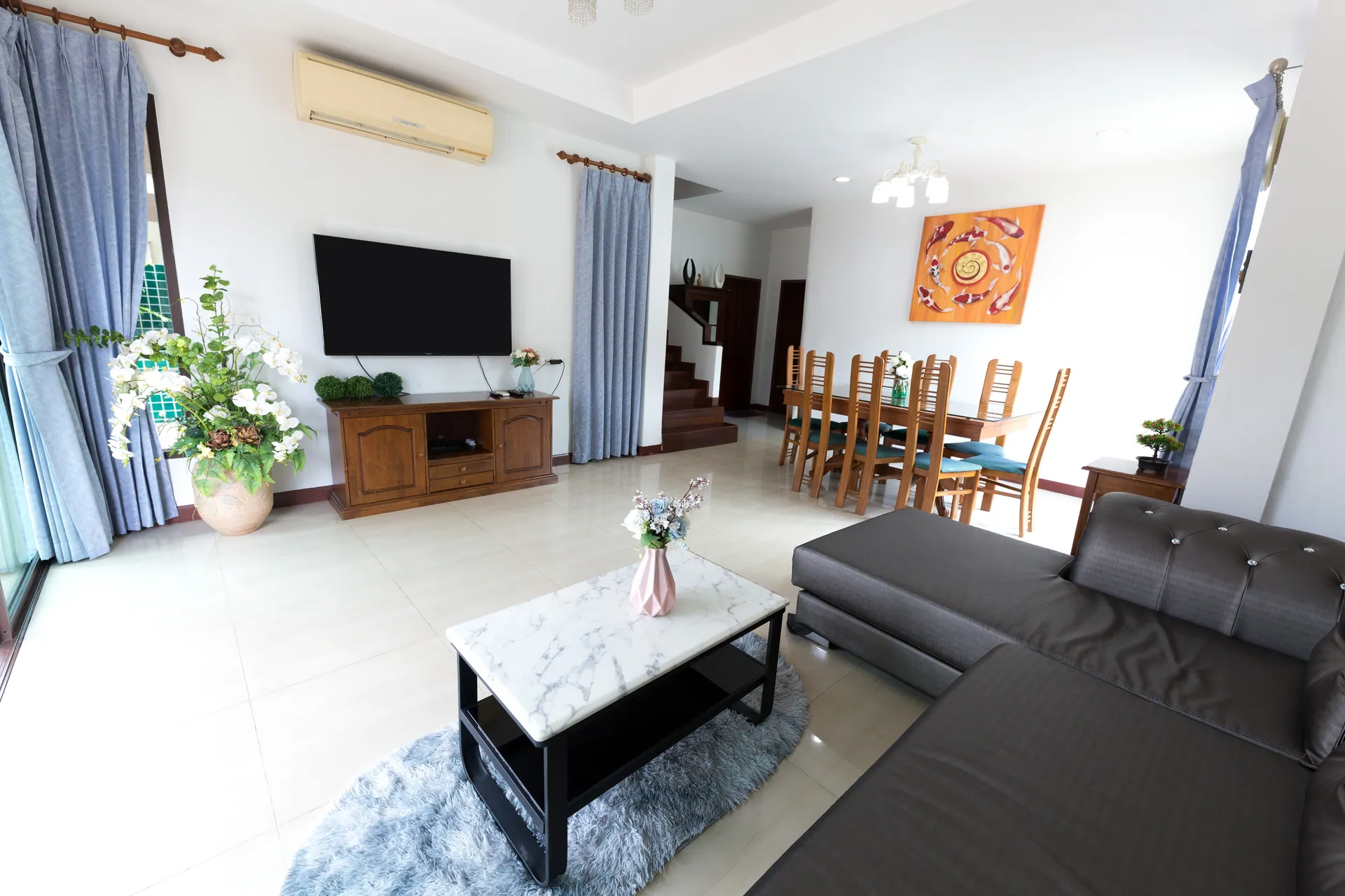 Open-plan living room with a grey corner sofa and marble coffee table, the dining table beyond
