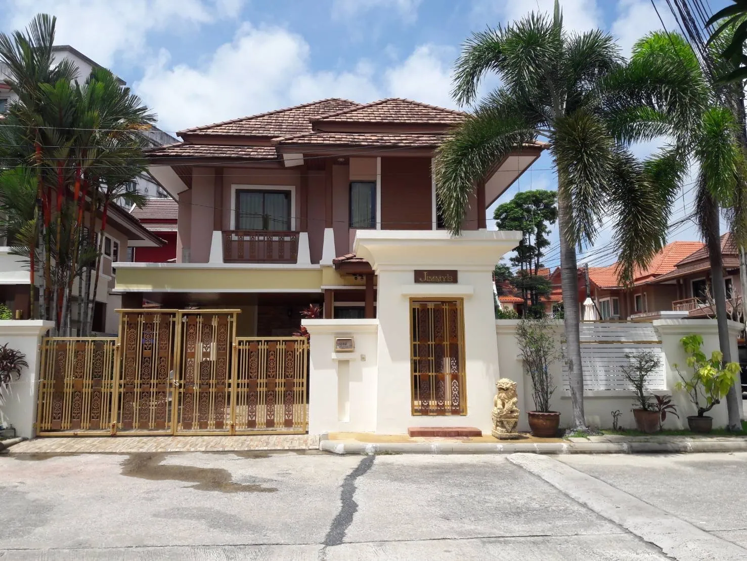 Front of the villa behind a cream wall and gate, on a paved lane lined with palms