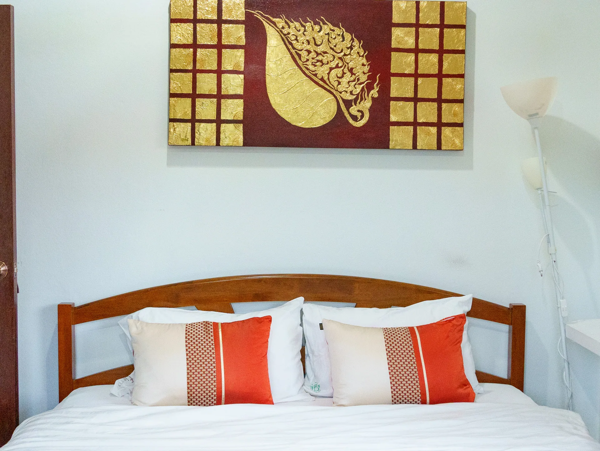 King bed with orange accent cushions below a red and gold leaf painting