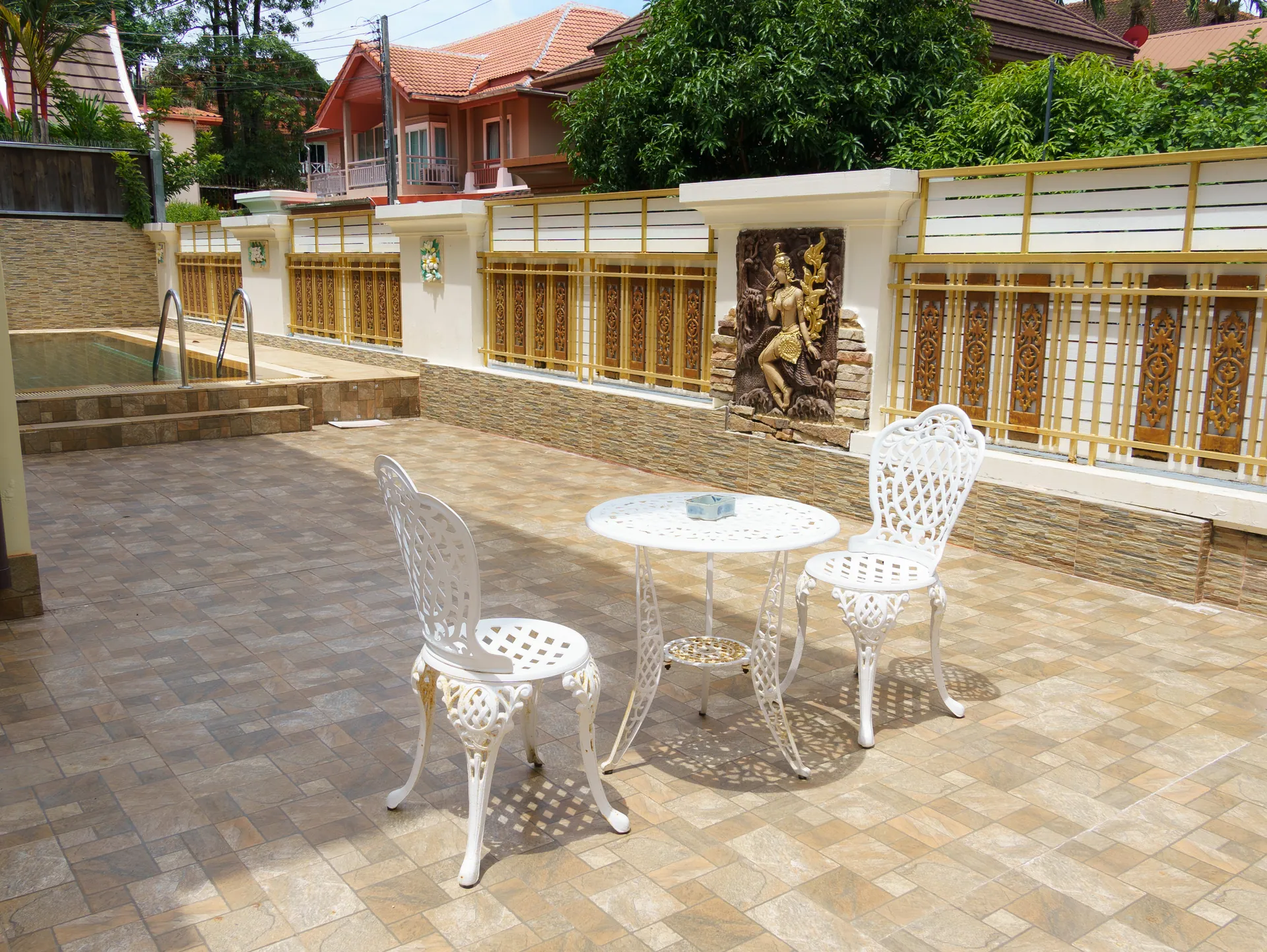 Paved pool terrace with a white wrought-iron table and chairs below a carved relief panel