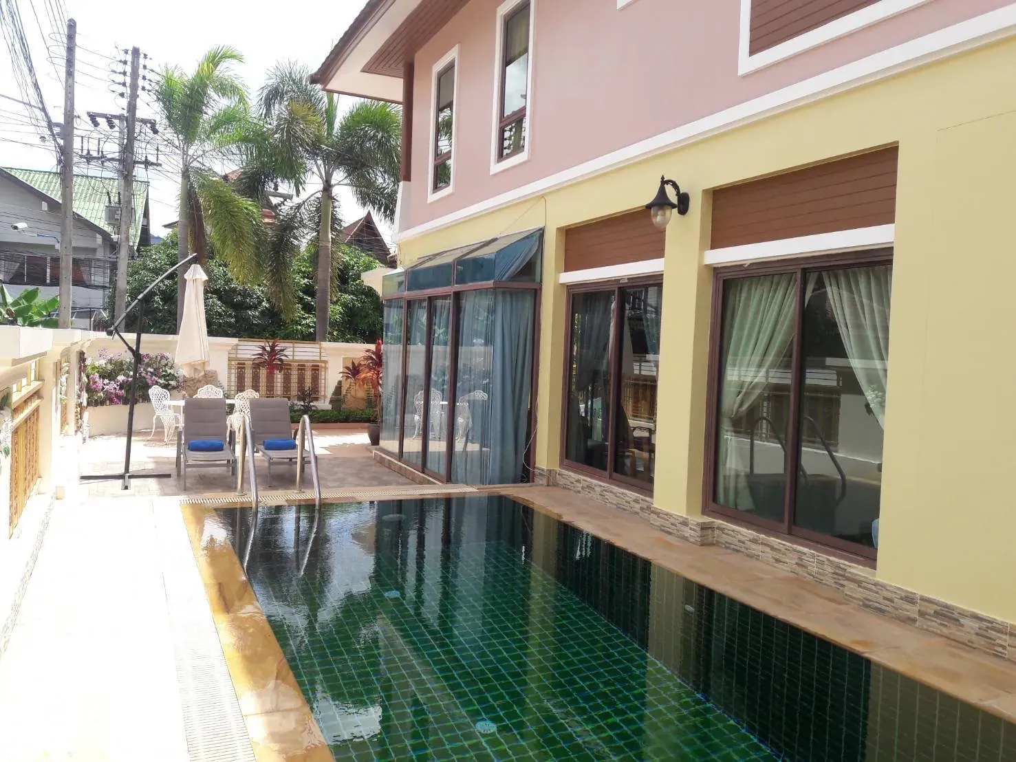 Pool beside the villa's glass doors, with sun loungers and a parasol on the terrace beyond