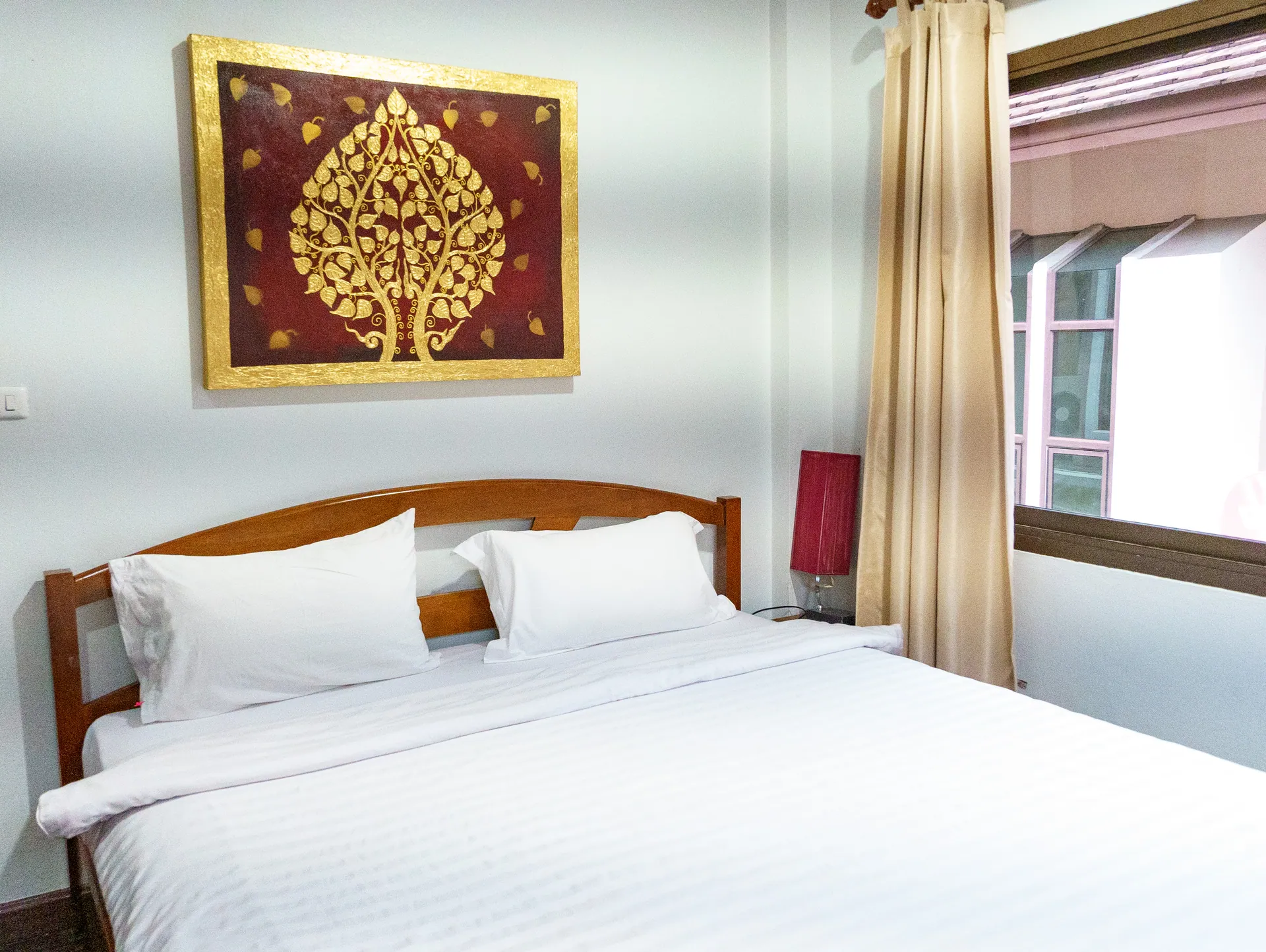 King bed with white linen below a red and gold bodhi tree painting