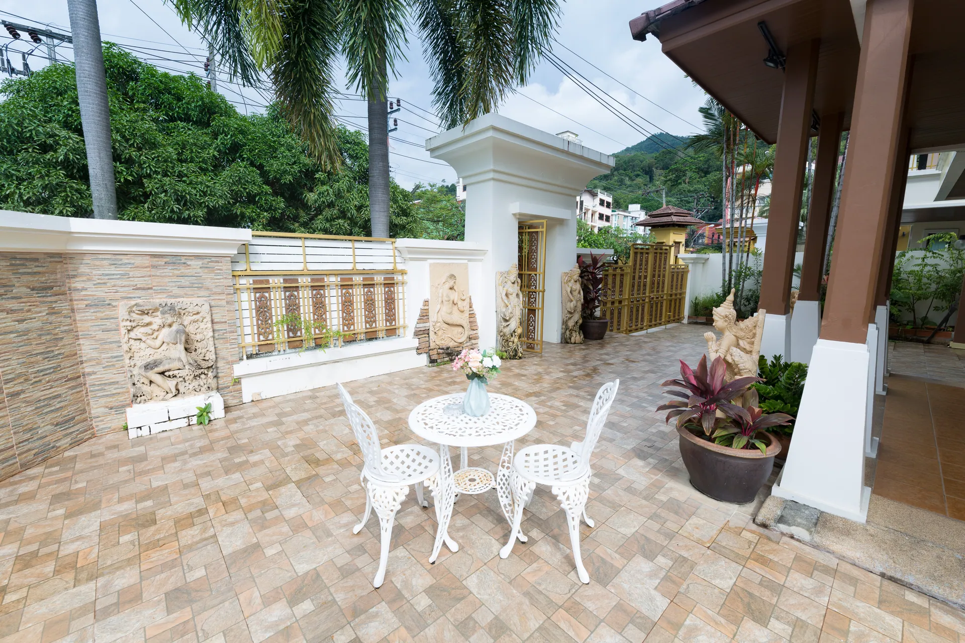 Garden terrace with a wrought-iron table set, potted plants and a carved gateway