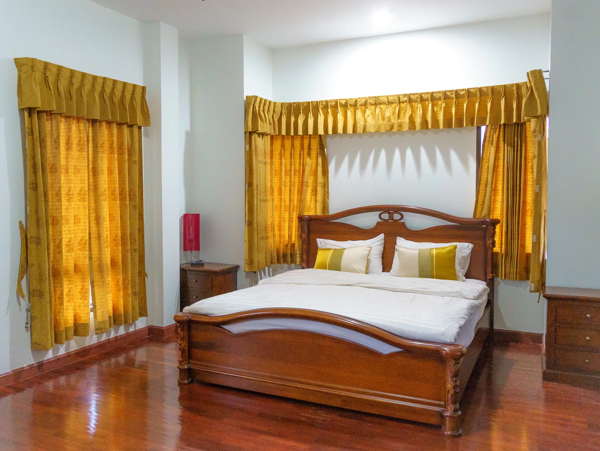 Bedroom with a carved wooden king bed, gold drapes and polished timber floors
