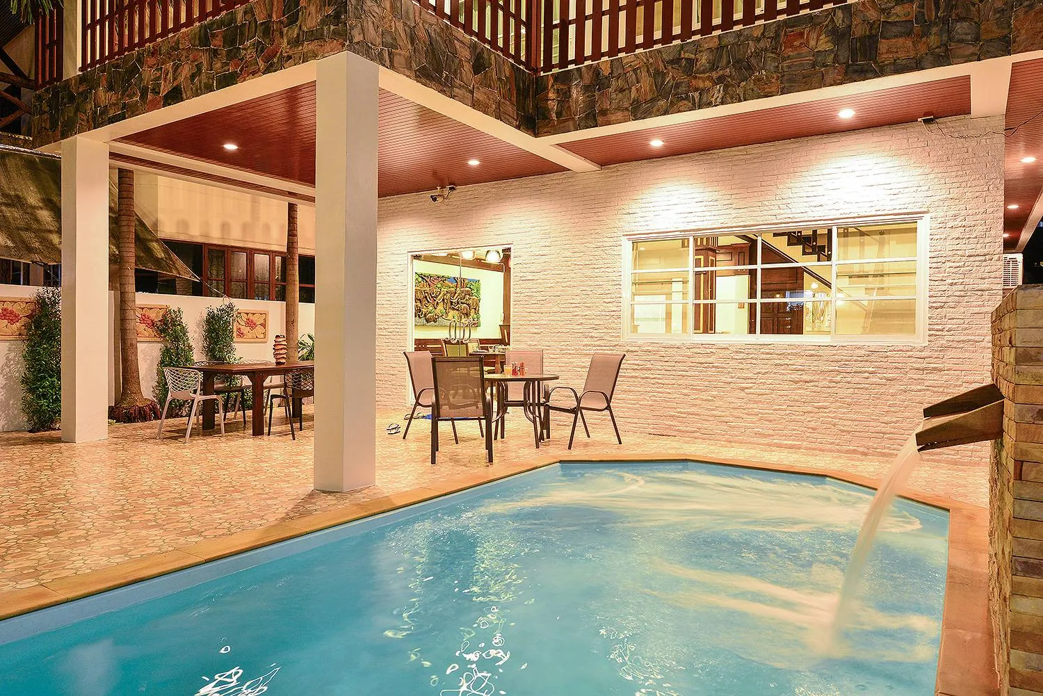 Private pool beside a covered terrace with dining tables, lit in the evening