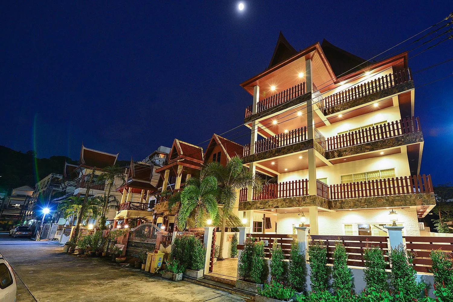 Four-storey villa with Thai-style gables and lit balconies at dusk, seen from the lane