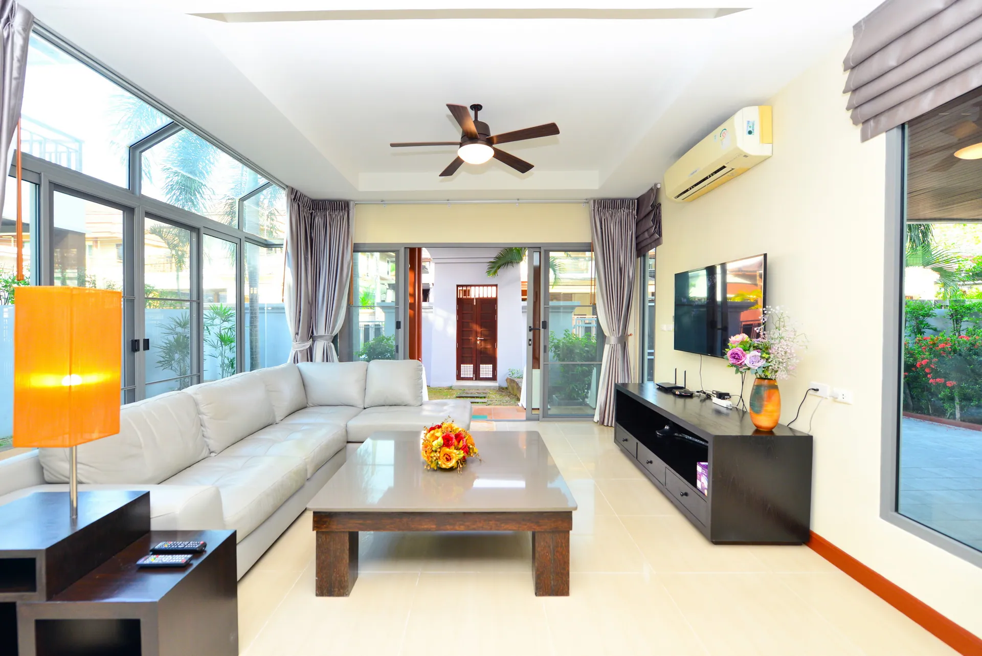 Living room with an L-shaped sofa, a ceiling fan, a TV and tall windows on two sides